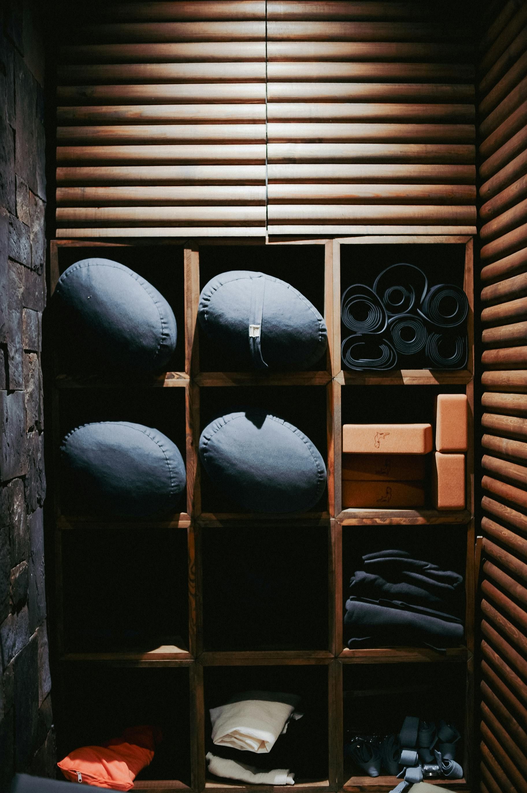 Des étagères en bois à casiers avec des vêtements pliés, des coussins bleus et un panier dans un espace ressemblant à un placard.