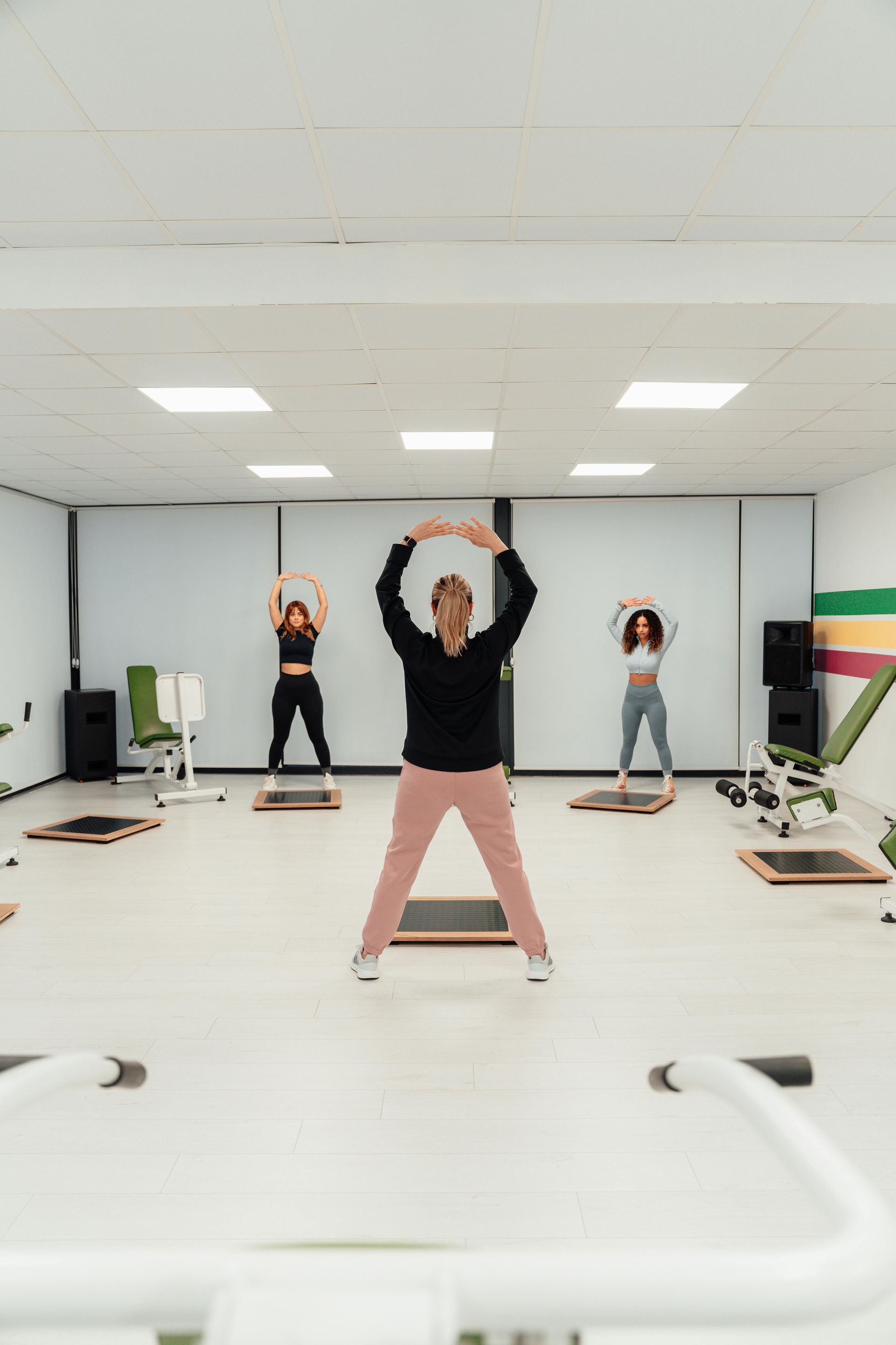 Trois personnes font des étirements en groupe dans un studio lumineux, les bras levés au-dessus de la tête.