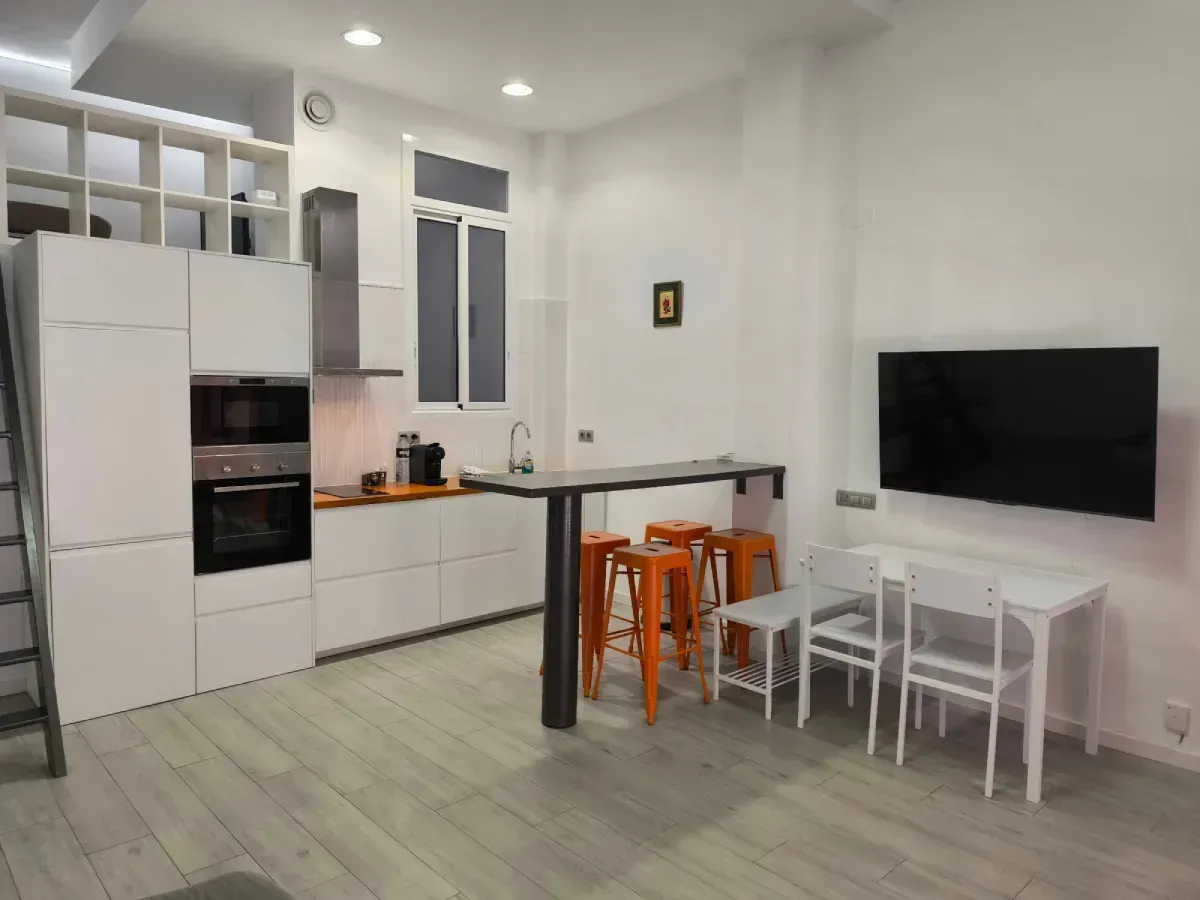 Cocina y sala de estar modernas con gabinetes blancos, encimeras negras, un televisor de pared