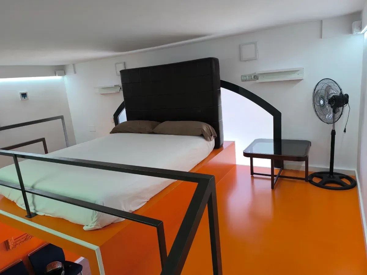 Dormitorio moderno con suelo naranja brillante, estructura de cama negra, ropa de cama blanca