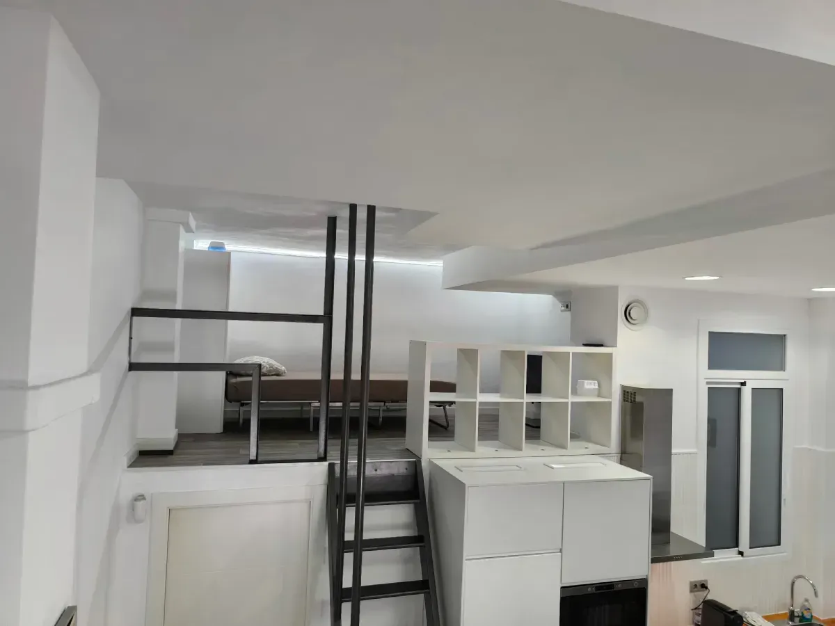 Interior tipo loft blanco con escalera negra, barandilla de altillo y estanterías empotradas.