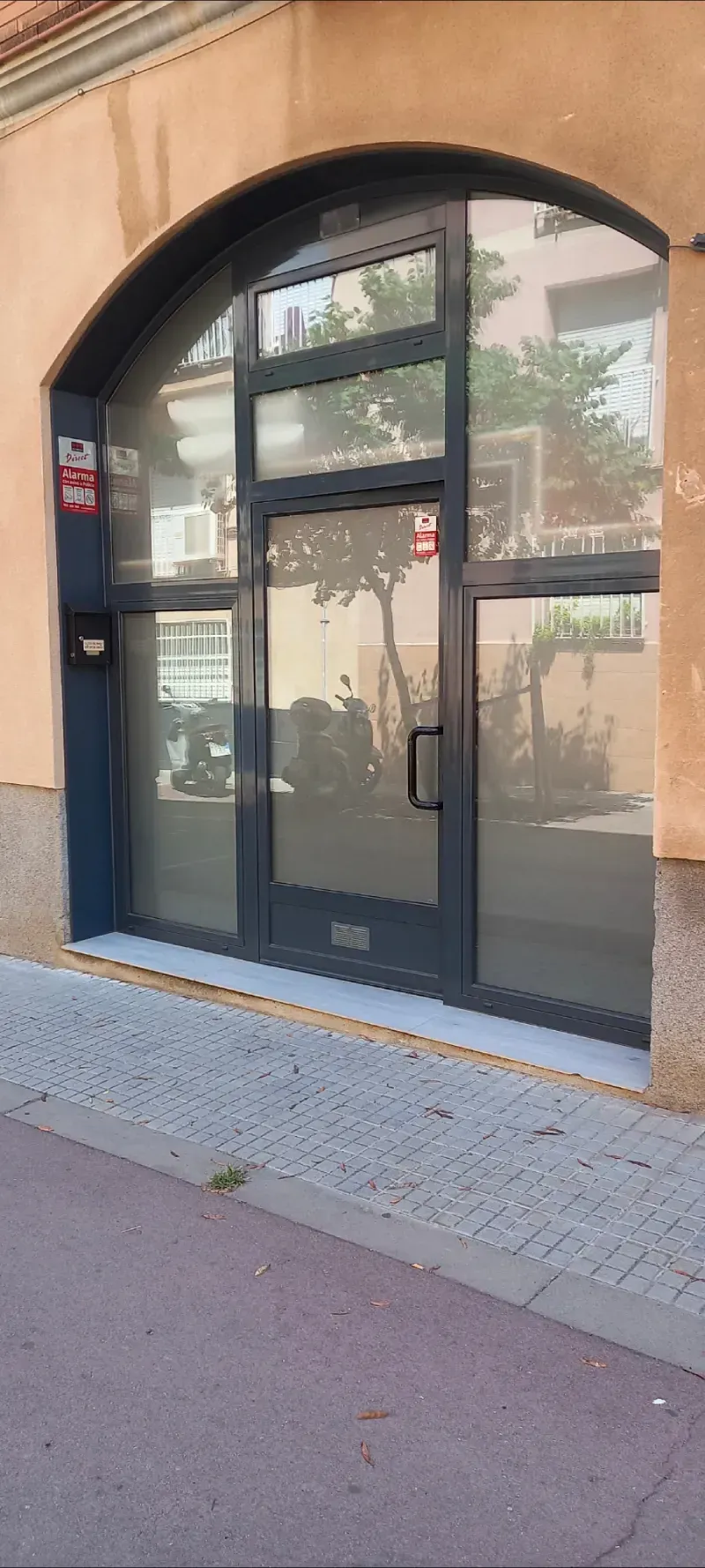 Entrada arqueada negra con puerta y ventanas de cristal en la fachada de un edificio de color beige.