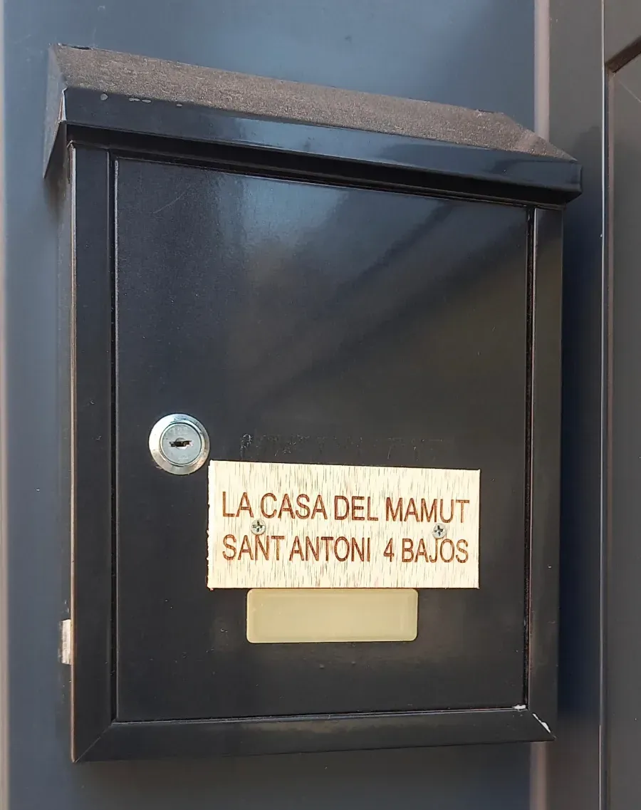 Buzón de pared negro con una pequeña etiqueta que dice “La Casa del Mamut Sant Antoni Abat”