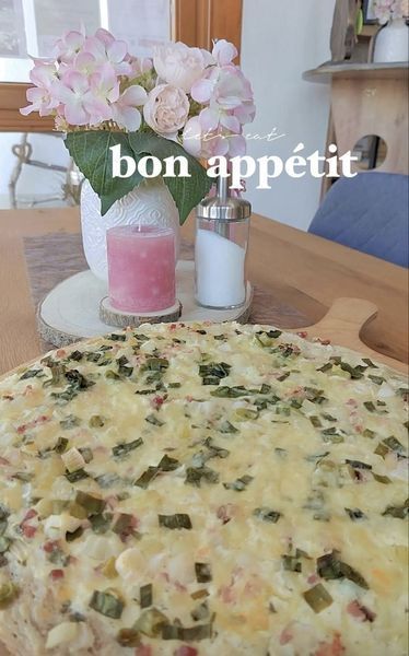 Flammkuchen auf einem Holzservierbrett und Osterdeko auf dem Tisch bestehend aus einer pinken Kerze, einem pinken Holzhasen und einer Blumenvase