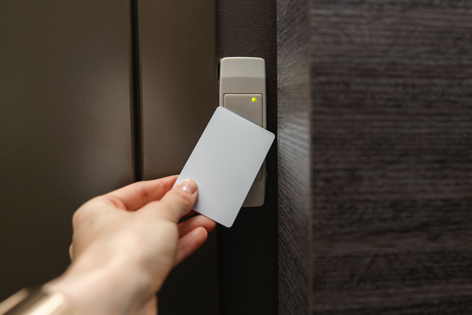 Main tenant une carte-clé blanche près d'un lecteur de carte de porte 