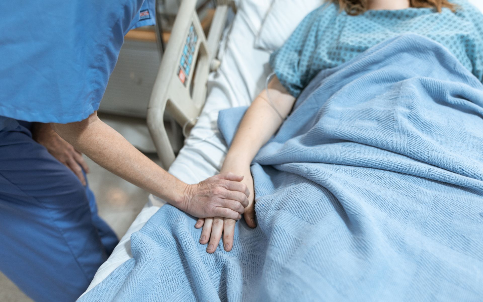 Una enfermera sostiene la mano de un paciente en una cama de hospital.