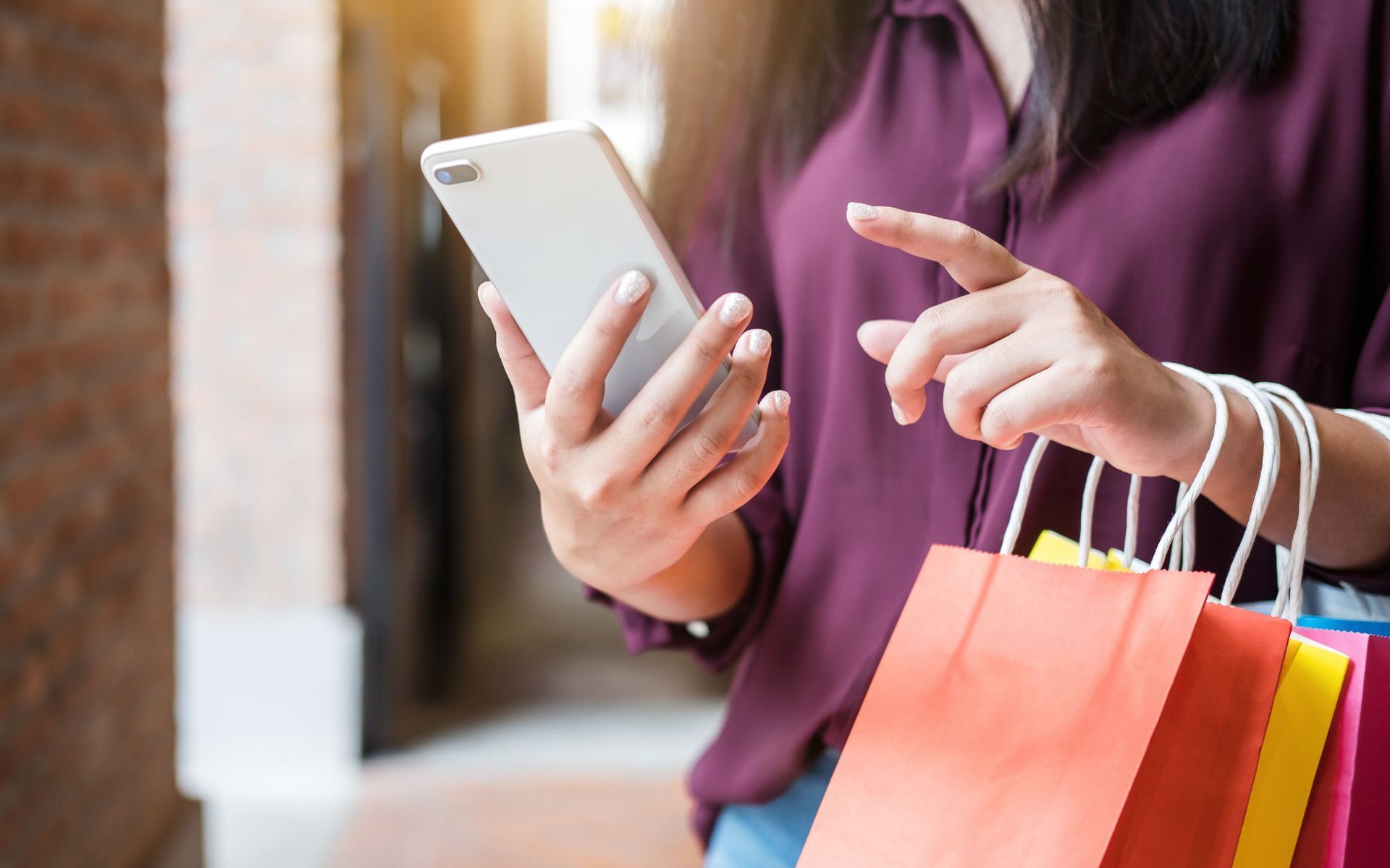 Una mujer sostiene bolsas de compras y usa un teléfono celular.