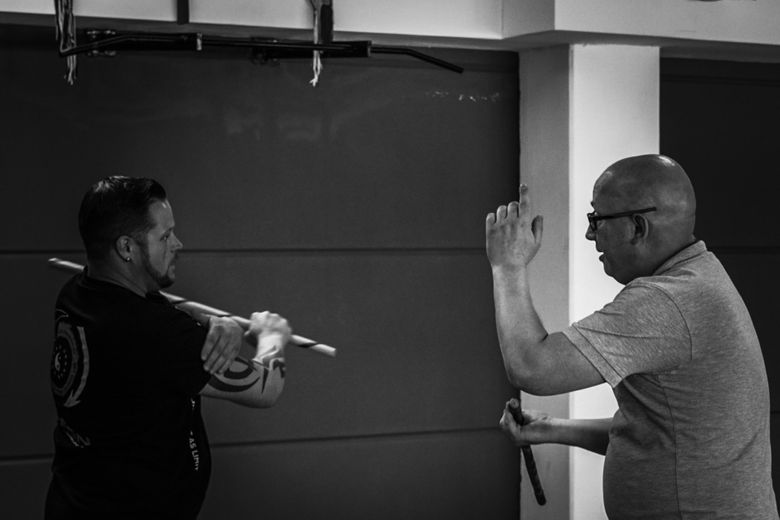 Ein Kampfsporttrainer demonstriert seinem Schüler die richtige Haltung des Stocks