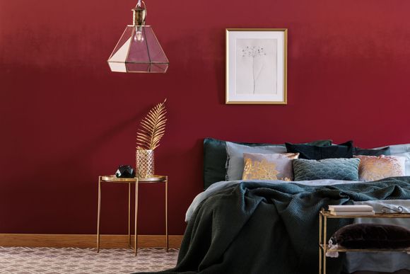 Une chambre aux murs rouges meublée d'un lit et une table de chevet
