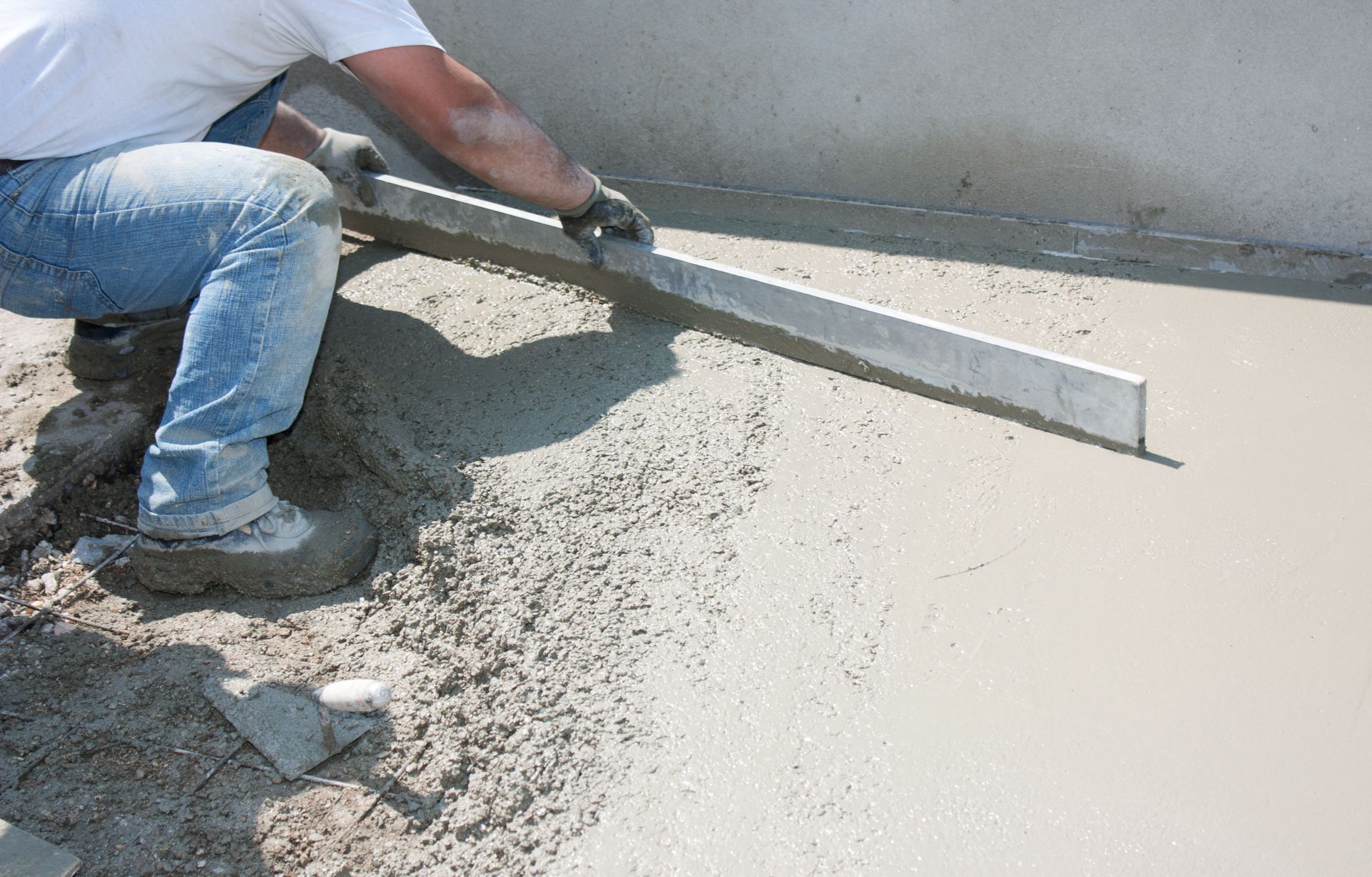 Un ouvrier nivelle du béton frais avec une longue règle sur un chantier de construction.