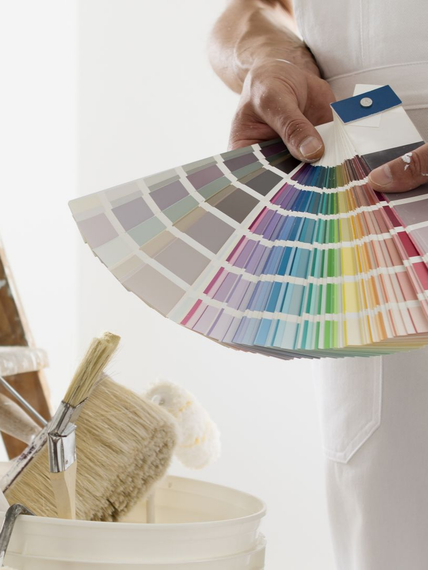 Une main tenant un éventail d'échantillons de peinture à côté de pinceaux et d'un pot de peinture.