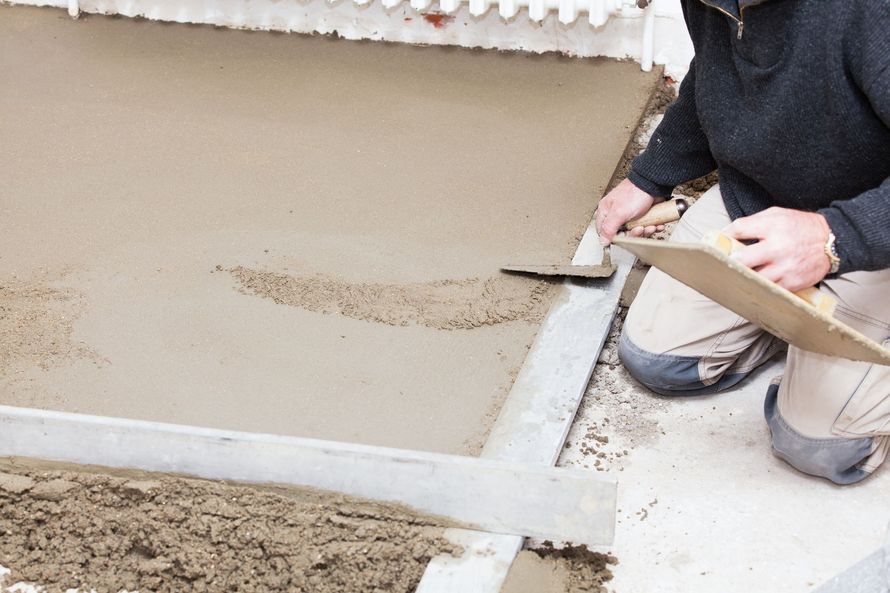 Un ouvrier lisse le béton frais le long d'une fondation à l'aide d'une truelle.