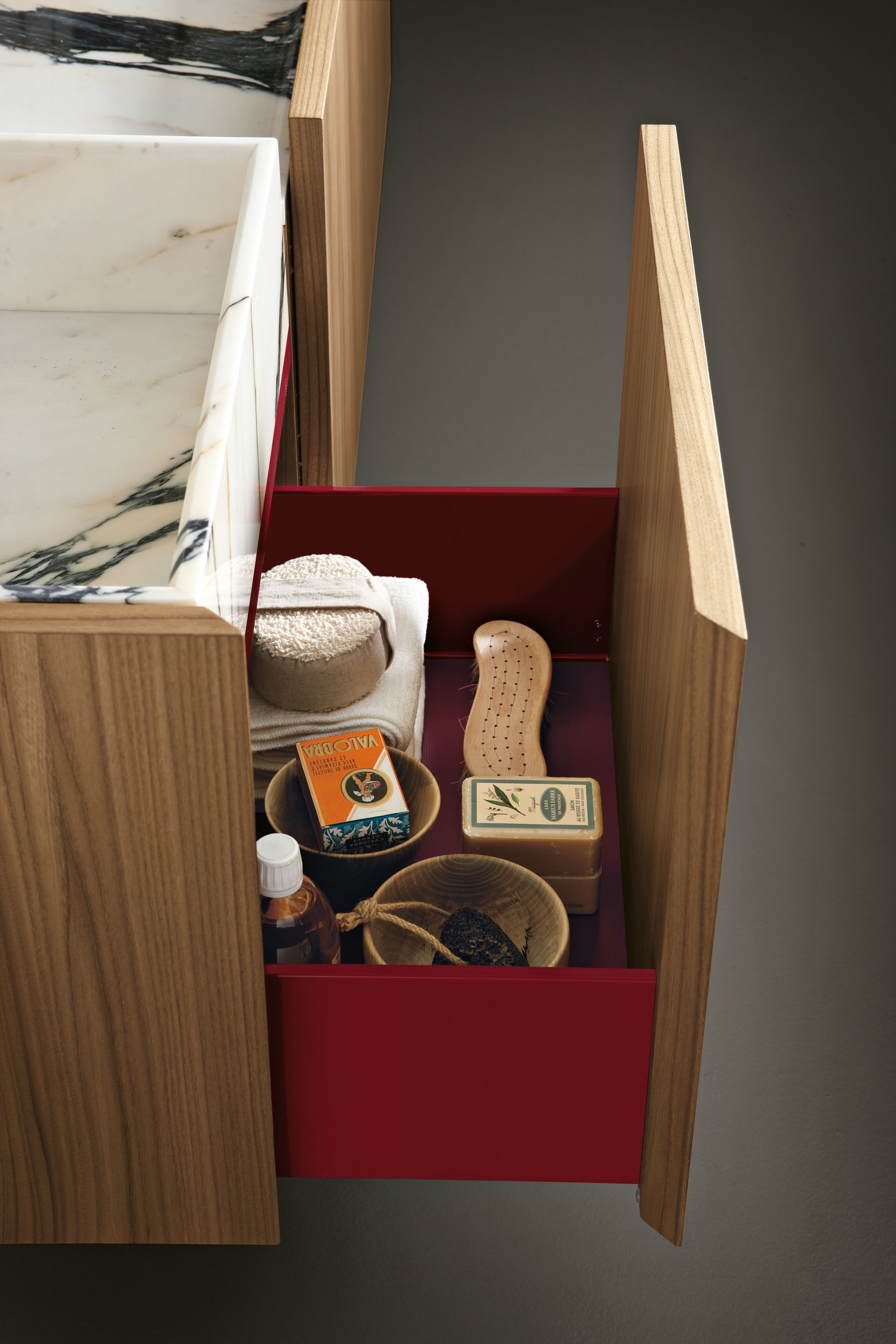 Ouvrir le tiroir rouge contenant des articles de toilette assortis et des petits récipients à côté d'un lavabo.