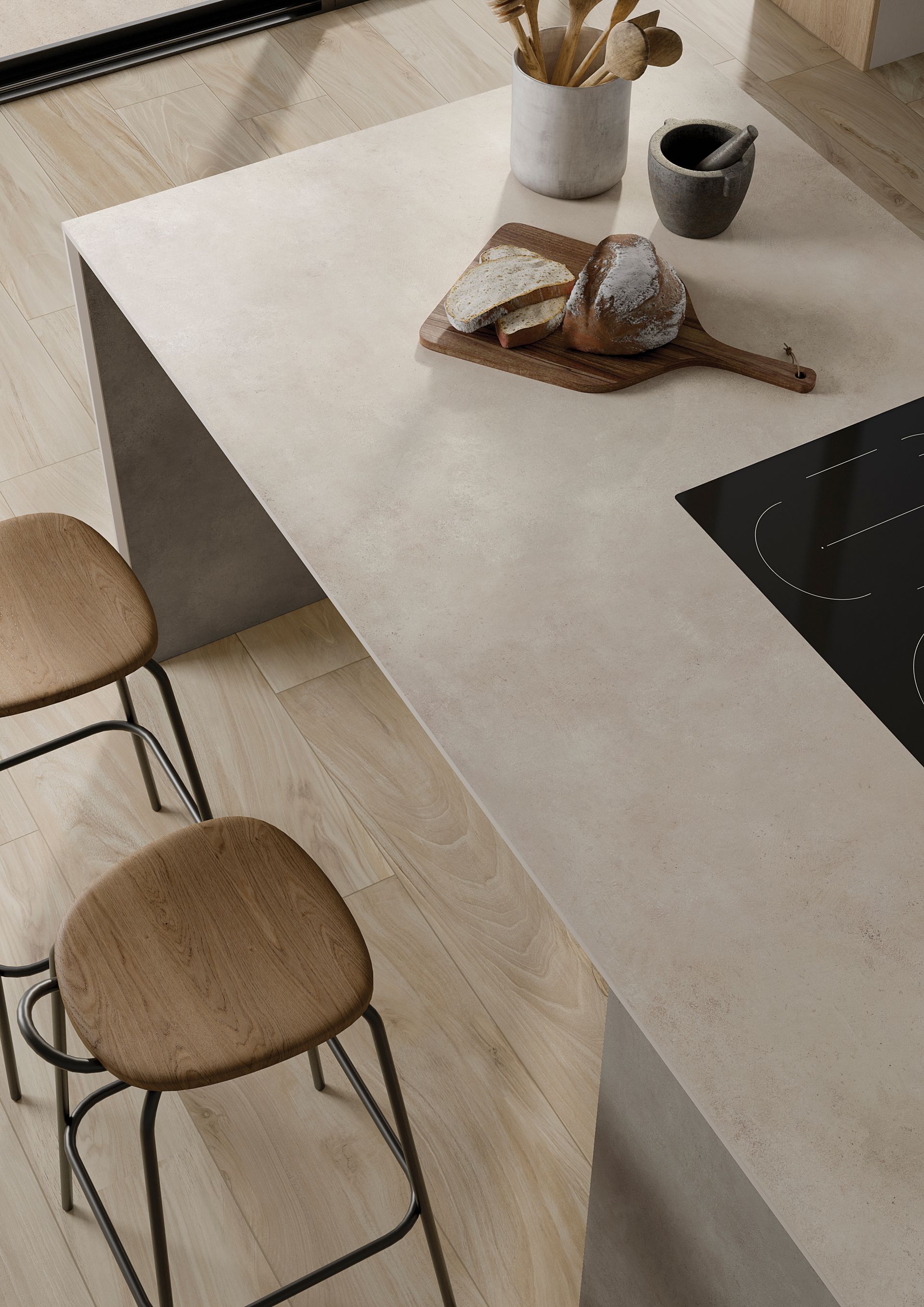 Îlot de cuisine moderne avec deux tabourets en bois, un plateau, un vase et une plaque de cuisson noire sur un sol clair.