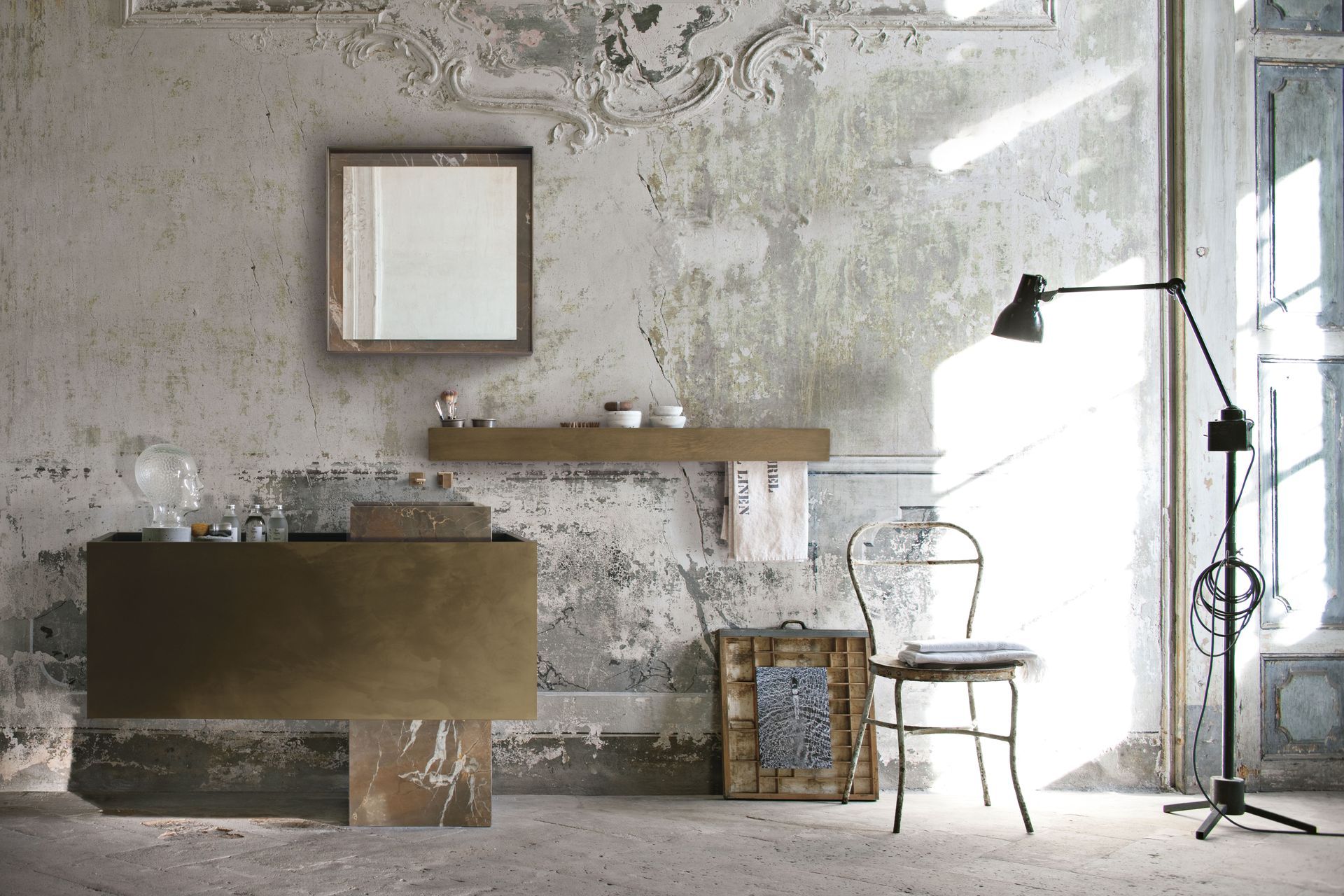 Pièce rustique minimaliste avec un mur vieilli, des tableaux encadrés, une étagère, une chaise, un lampadaire et la lumière du soleil provenant d'une fenêtre.