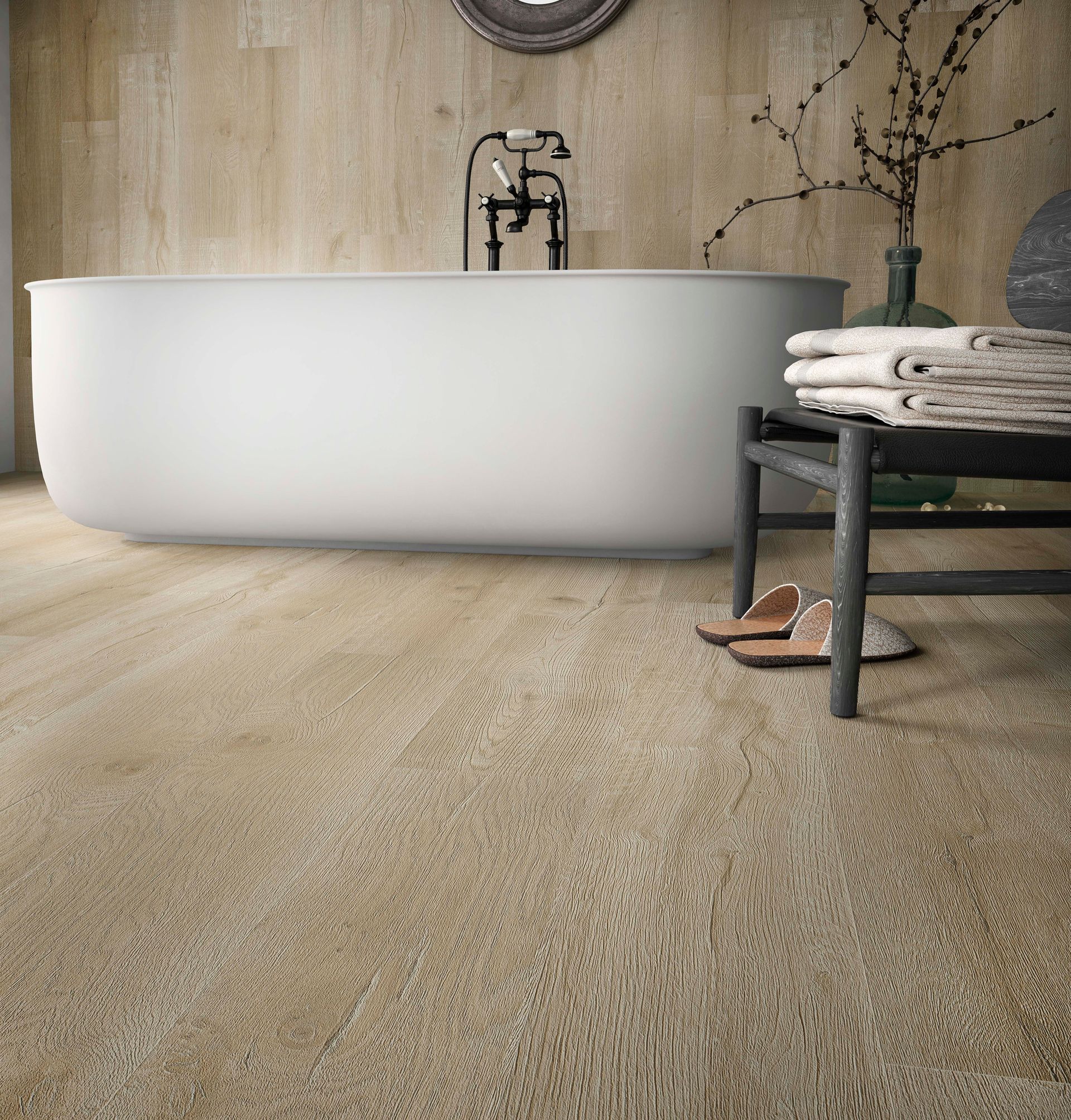 Salle de bains moderne avec baignoire blanche sur pieds, sol texturé beige et tabouret noir avec serviettes pliées.