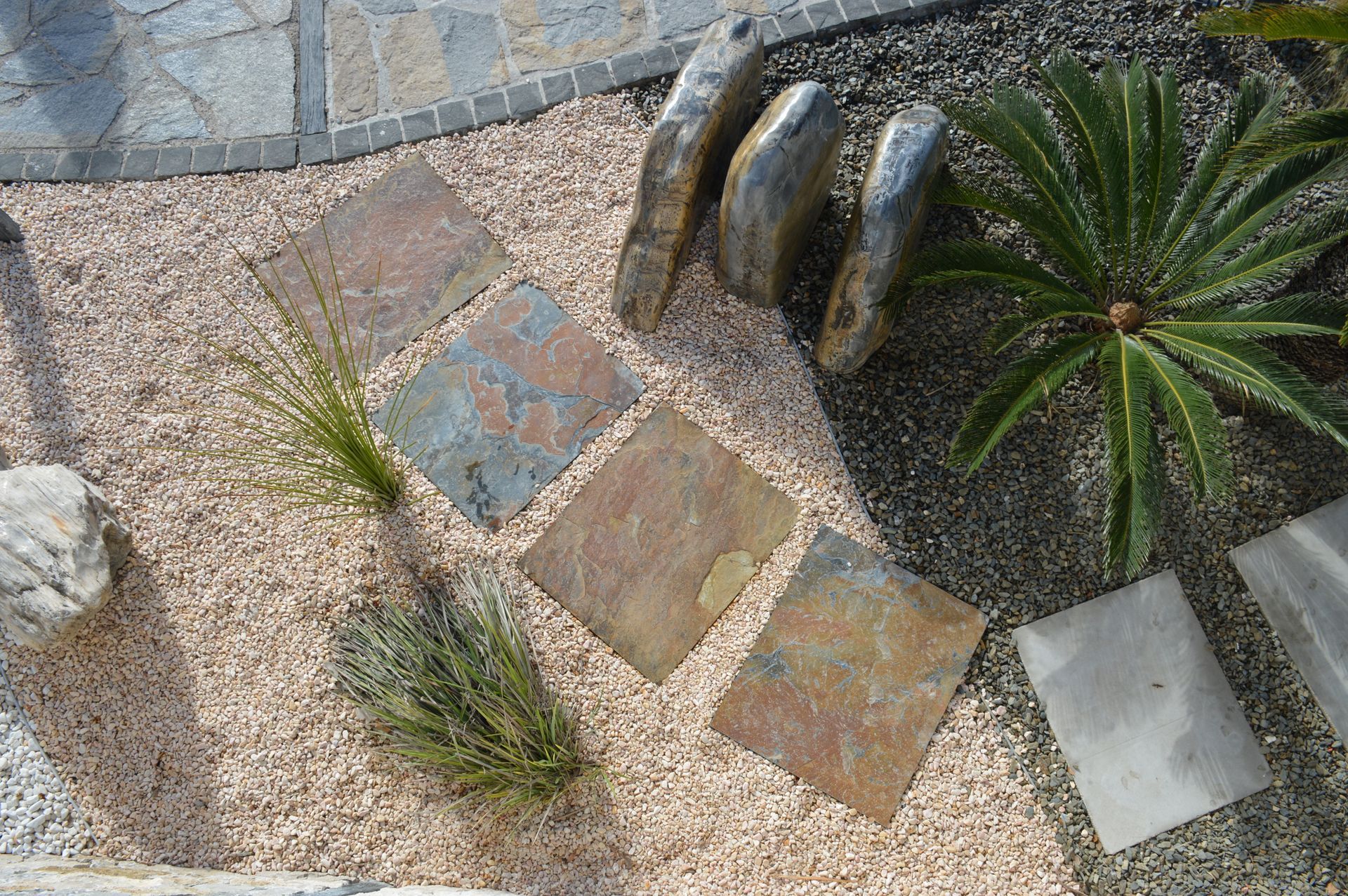 Allée incurvée en pierre avec galets, petites plantes et sculpture décorative en métal dans un patio de jardin
