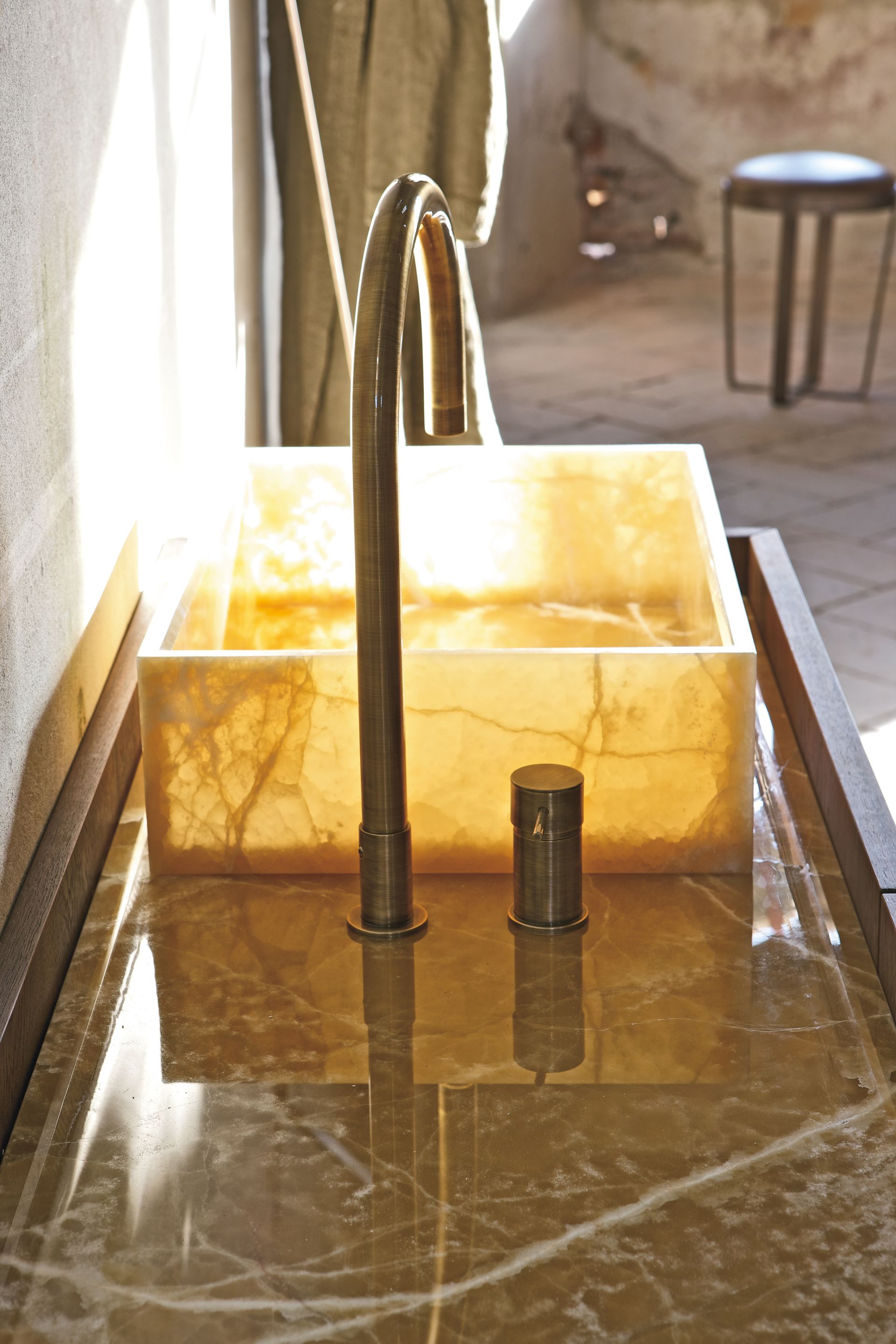 Lavabo en marbre avec robinet en métal brossé et vasque carrée en pierre jaune près d'une fenêtre