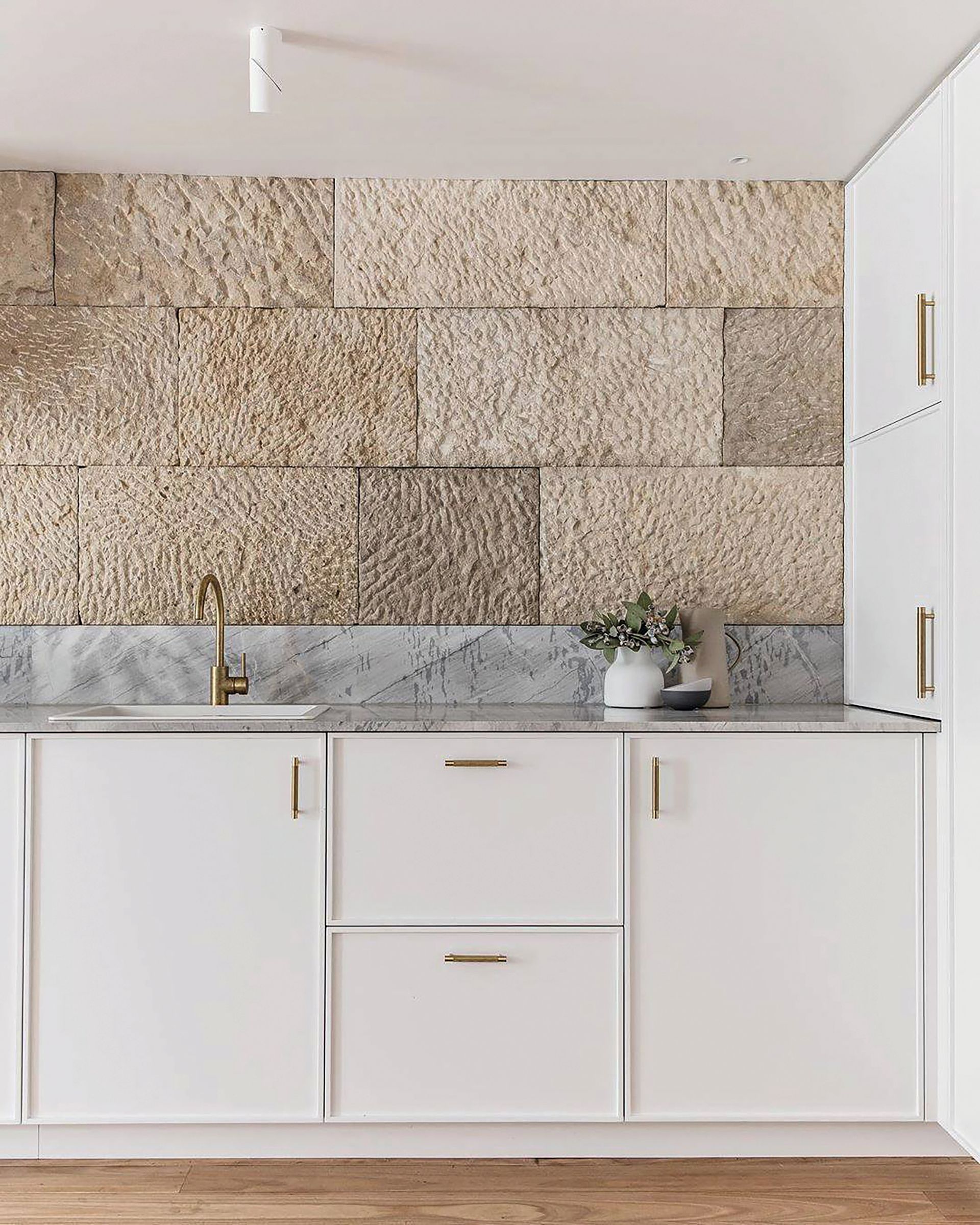 Meubles blancs minimalistes et crédence en pierre dans une alcôve de cuisine moderne et lumineuse