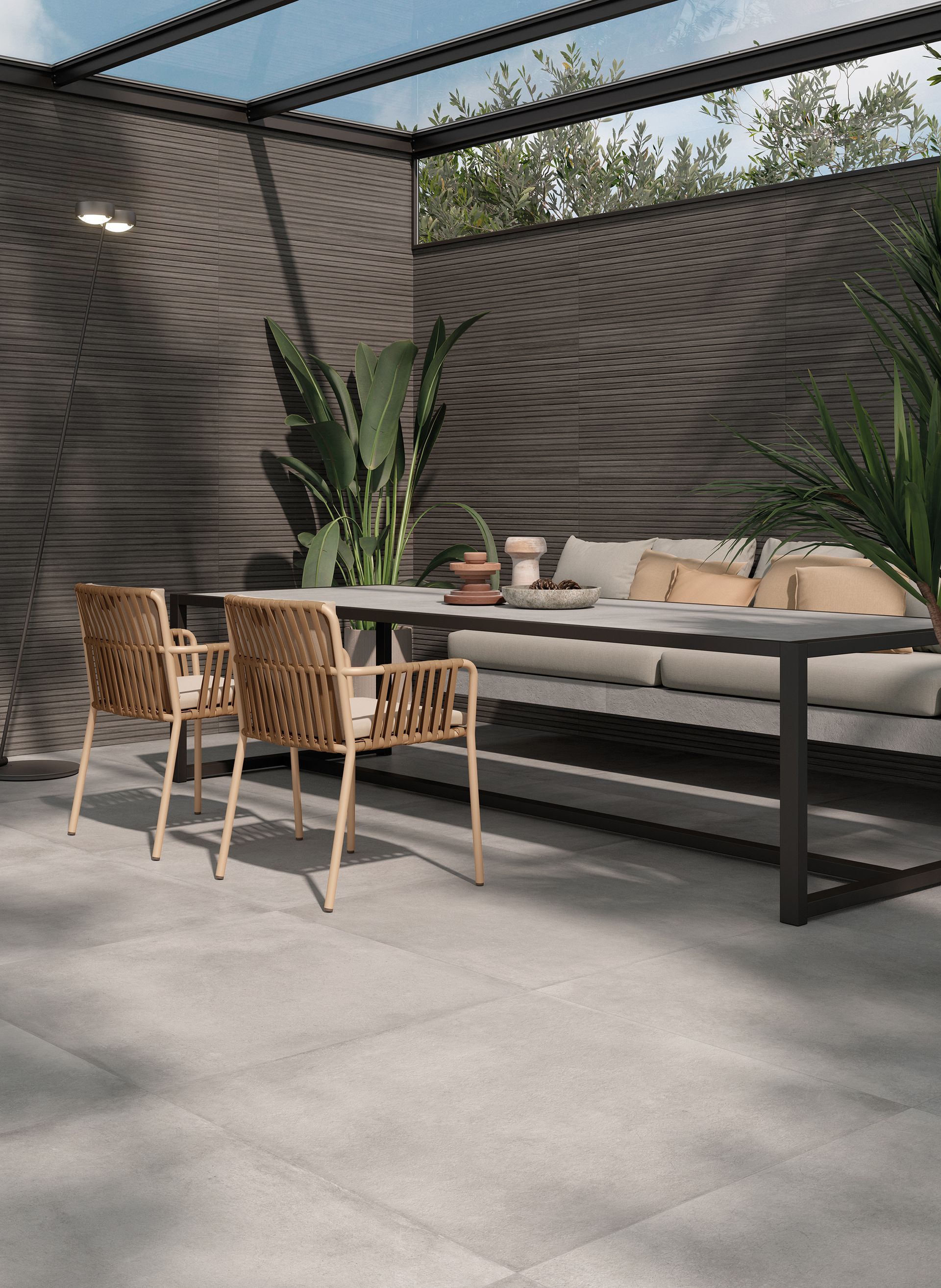 Terrasse moderne aménagée avec chaises en osier, une longue table et des plantes en pot sous une pergola à claire-voie.