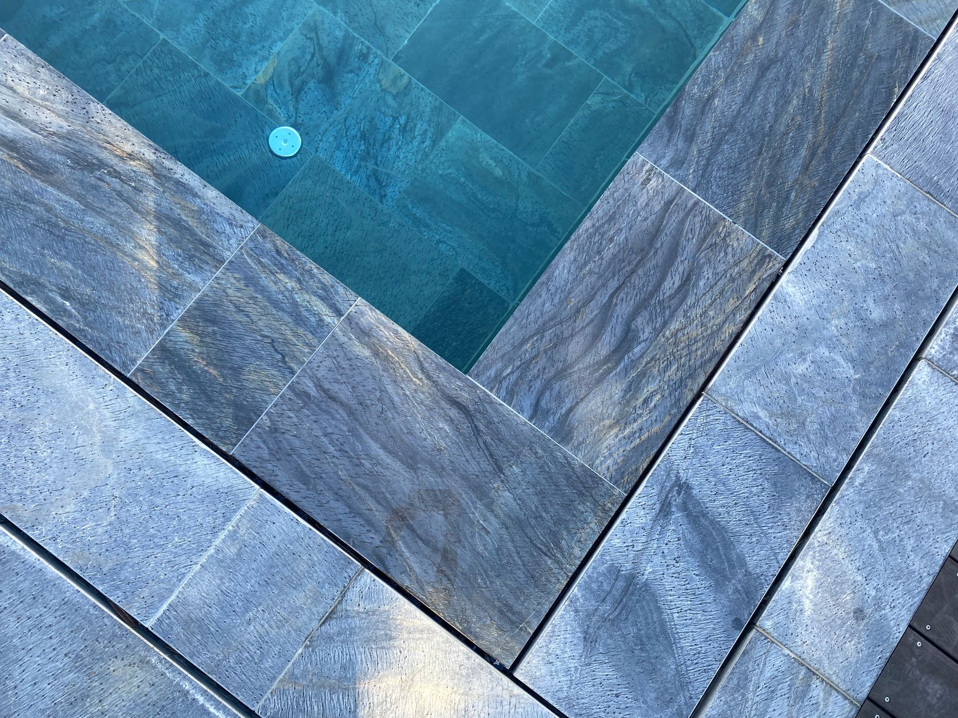 Des carreaux de pierre bleu-gris à chevrons encadrent un petit bassin d'eau turquoise.