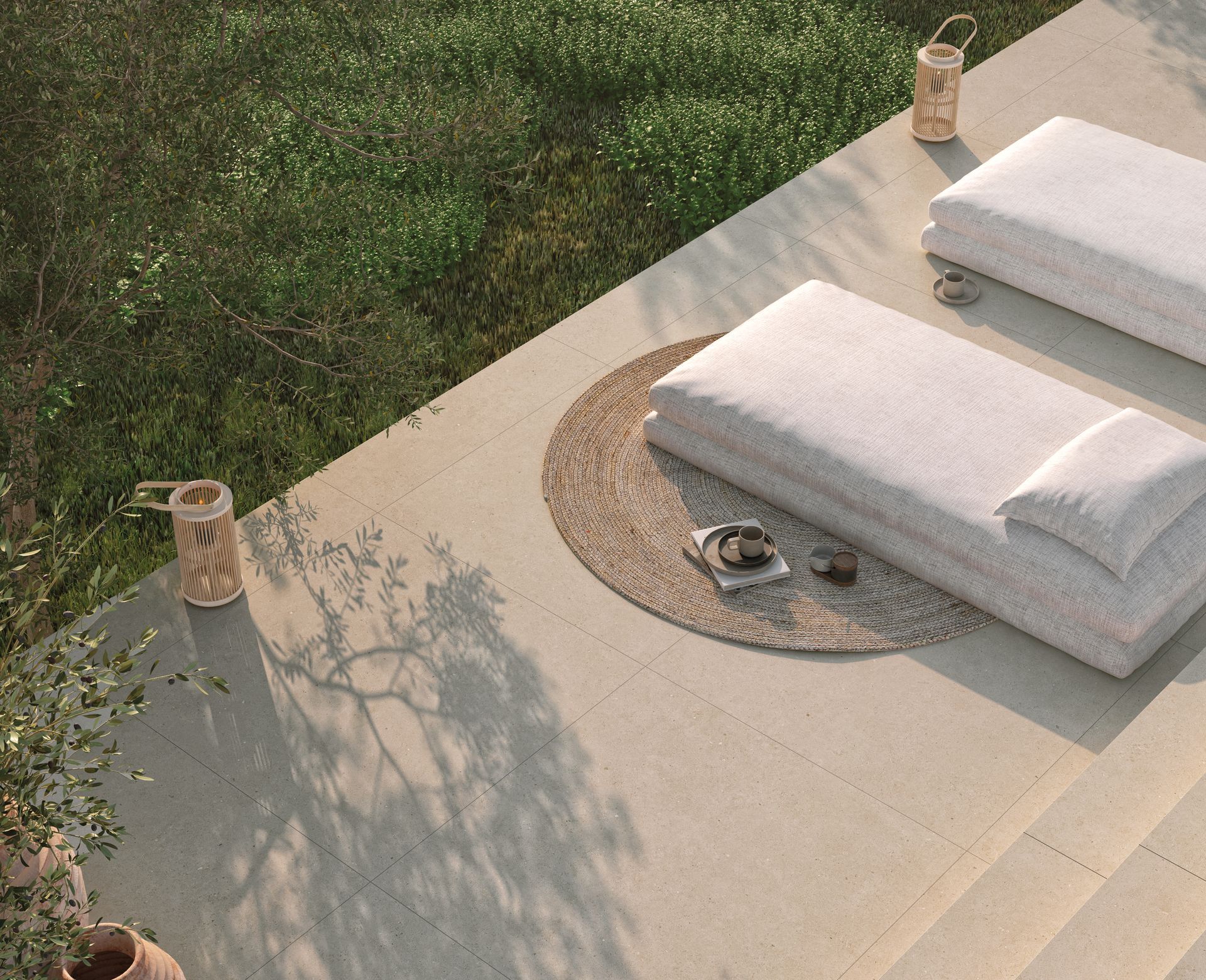 Aménagement d'un spa extérieur avec des serviettes blanches sur un tapis, des bougies et un plateau tressé sur de l'herbe et des pierres.