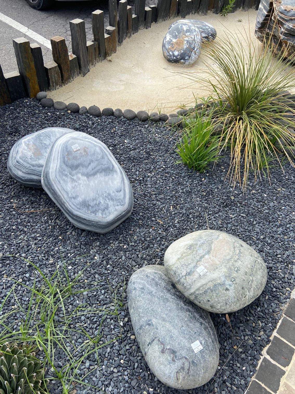 Roches décoratives et graminées dans un parterre de jardin paysager avec gravier et bordure en bois