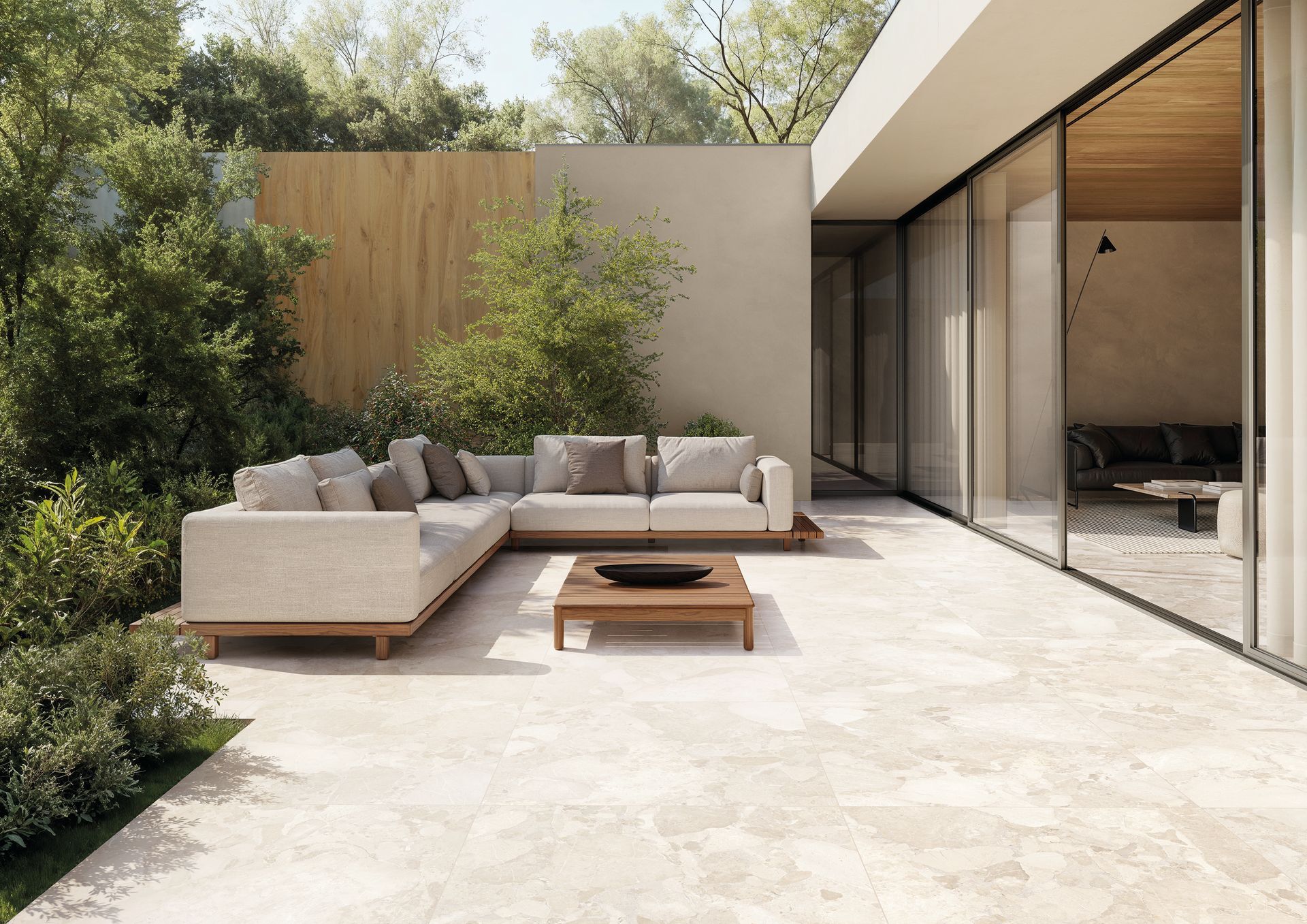 Terrasse moderne avec canapé d'extérieur beige, table basse et portes coulissantes en verre donnant sur une végétation luxuriante.