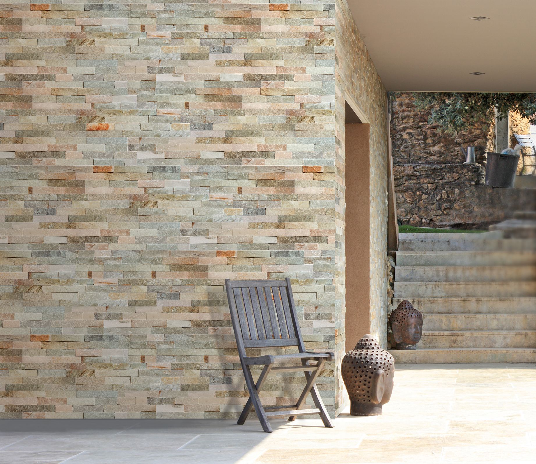 Terrasse en pierre avec une chaise en bois, un vase décoratif et des marches menant à un mur de jardin.