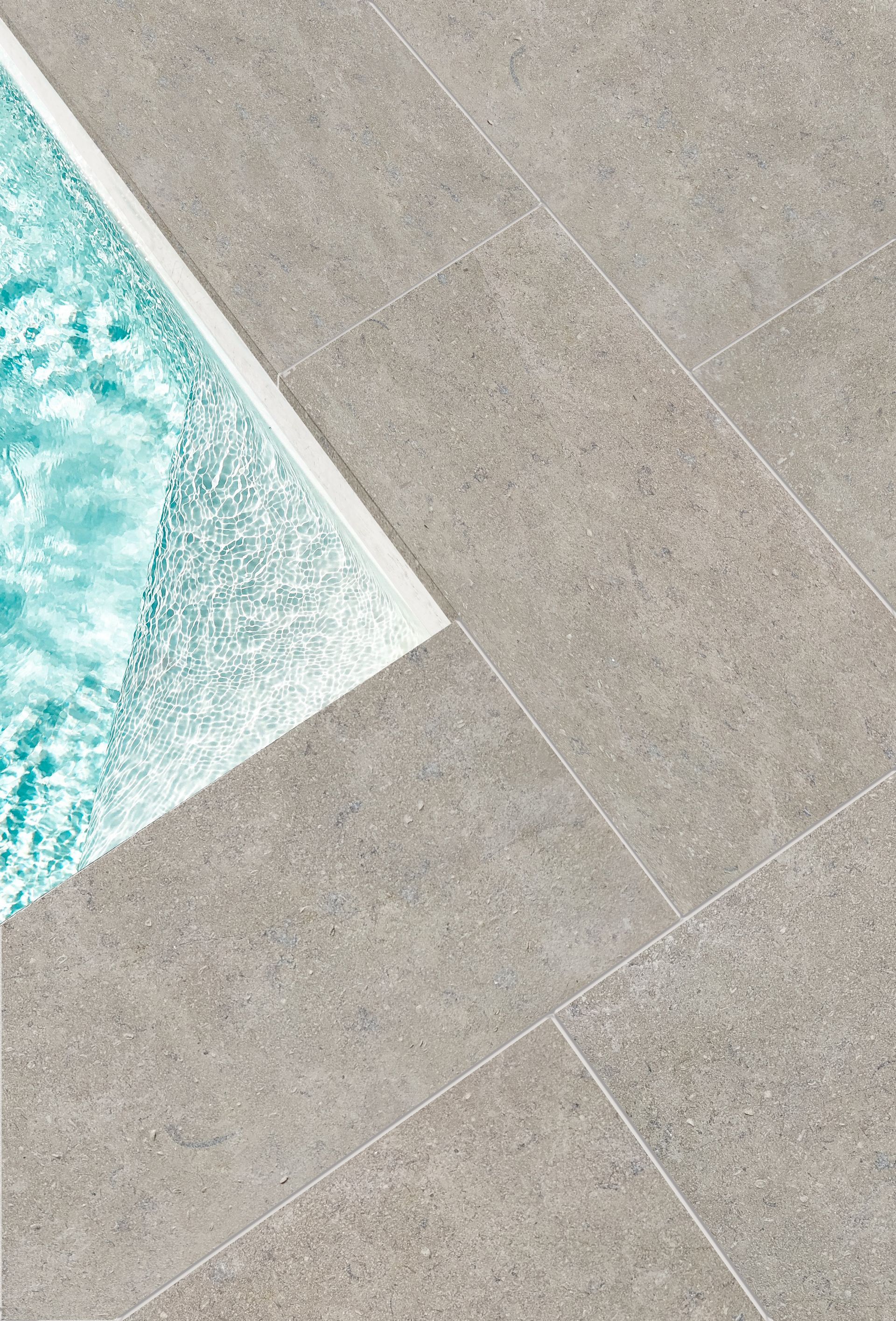 Vue en diagonale de l'eau turquoise de la piscine à côté de carreaux de pierre grise