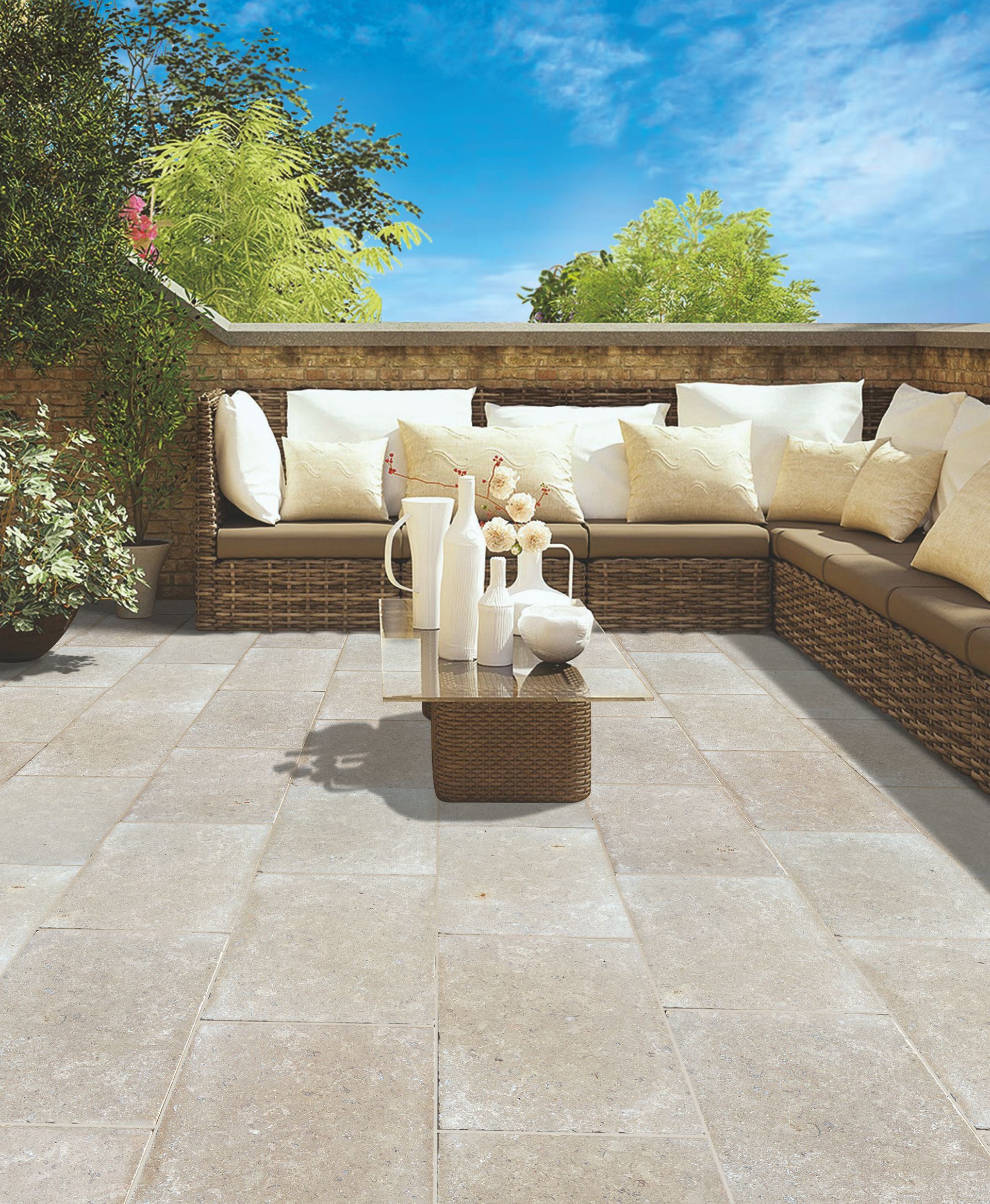 Terrasse extérieure avec canapé d'angle en osier, coussins couleur crème et petite table sous un ciel d'un bleu éclatant.