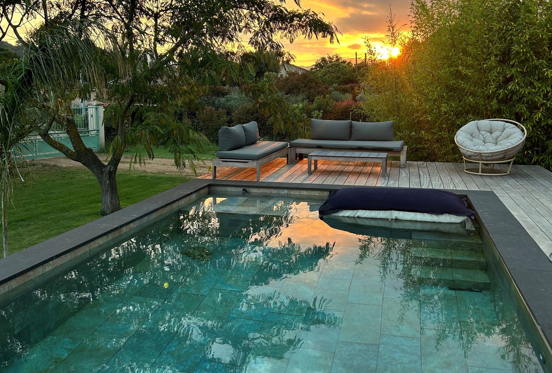 Piscine dans le jardin au coucher du soleil, avec chaises longues et arbres se reflétant dans l'eau