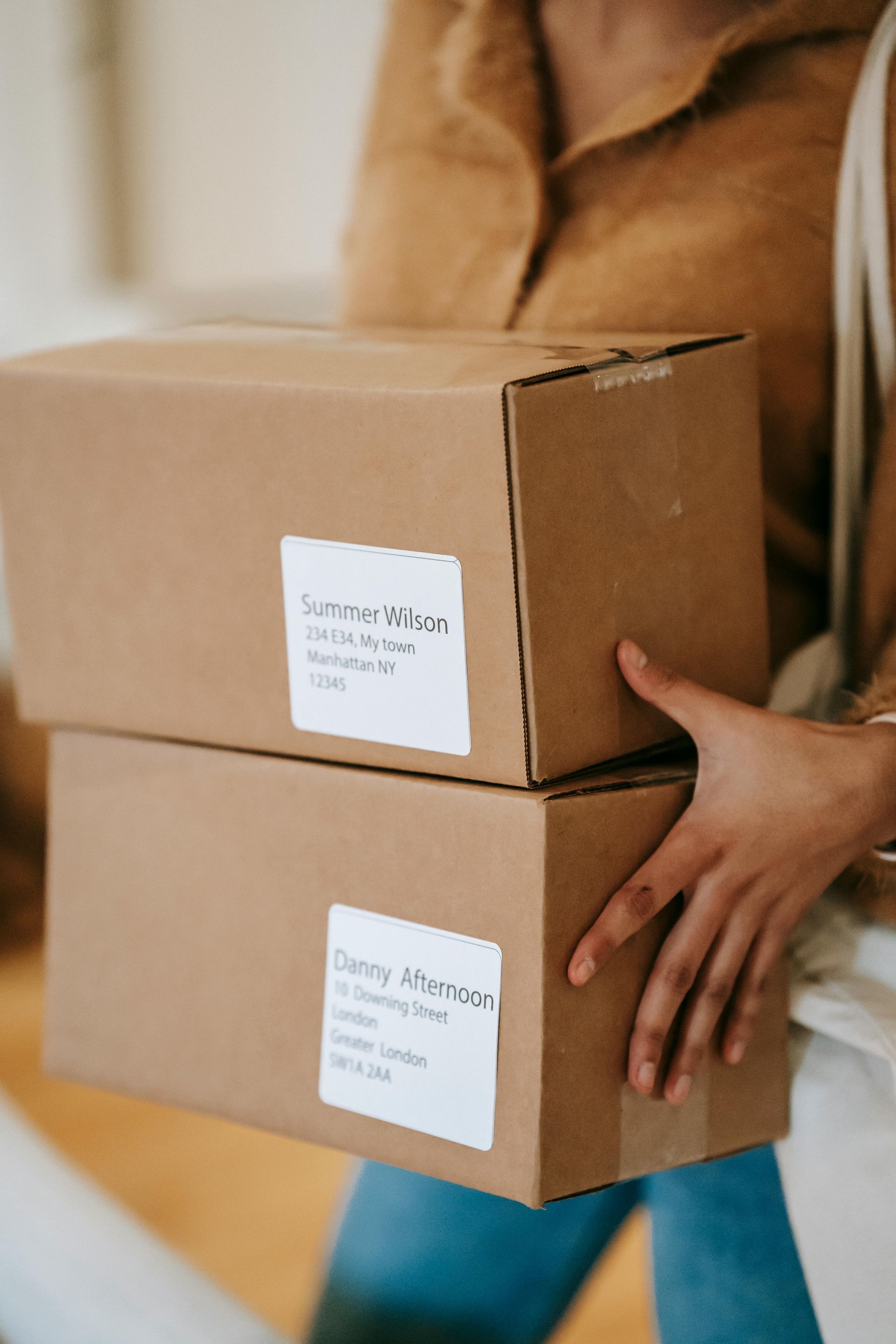 Persona que lleva dos cajas de cartón precintadas con cinta adhesiva al interior de una vivienda.