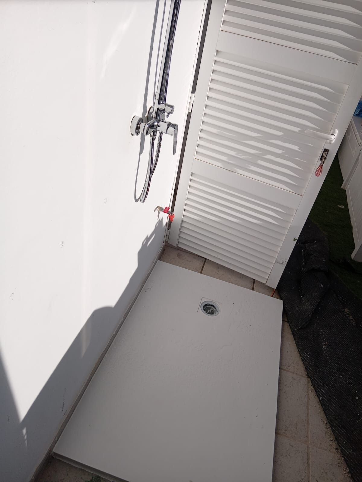 Una cabina de ducha blanca con un grifo rojo y una puerta blanca.