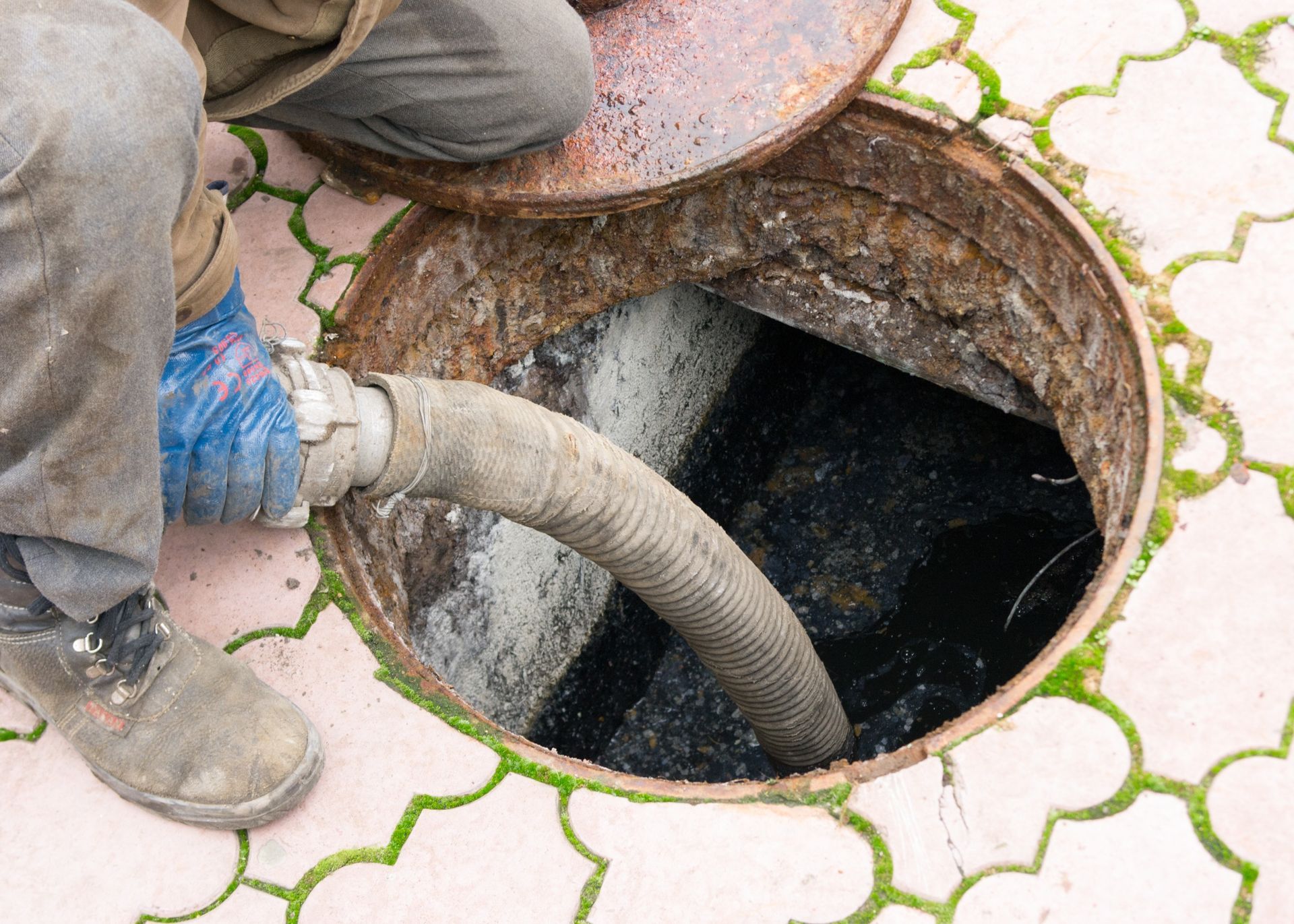 Un hombre está bombeando agua hacia una tapa de alcantarilla con una manguera.