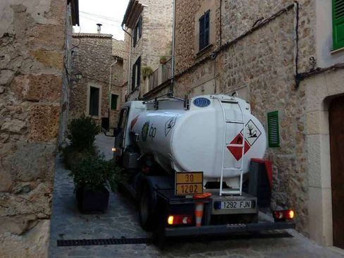 Un camión cisterna está estacionado en un callejón estrecho entre dos edificios de piedra.