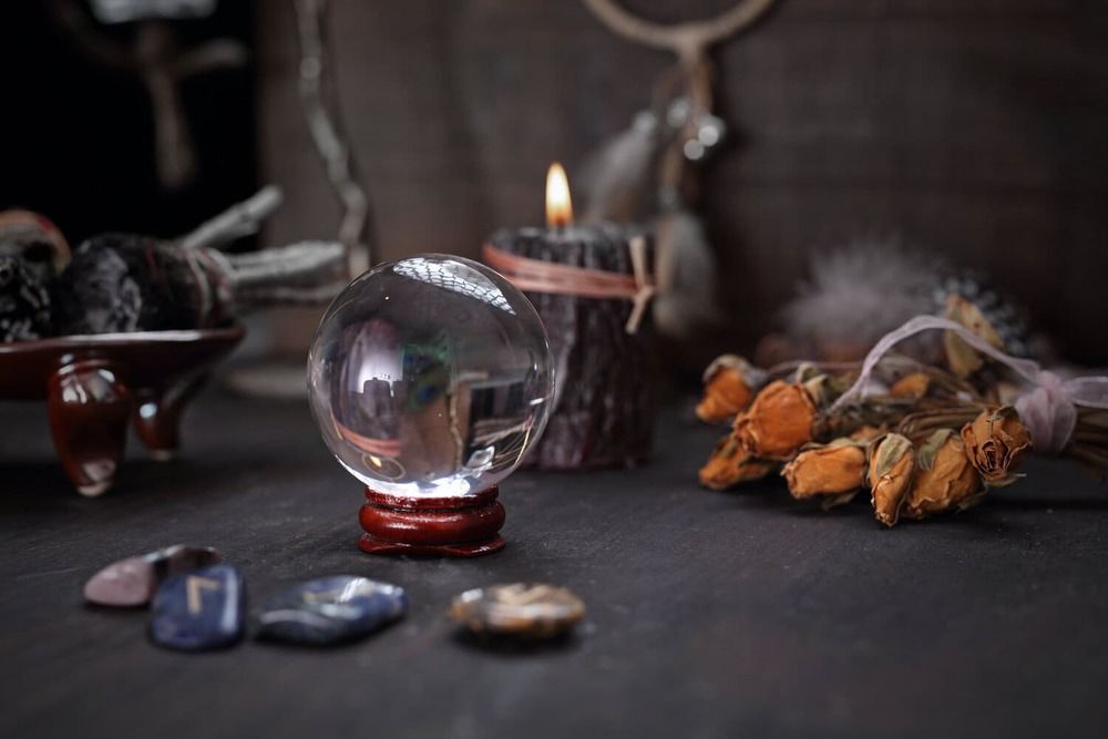 Bola de cristal sobre soporte de madera con vela encendida, hierbas secas y cristales.