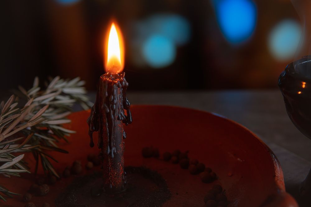 Vela negra encendida en un plato naranja, ramita de romero cerca, fondo borroso.