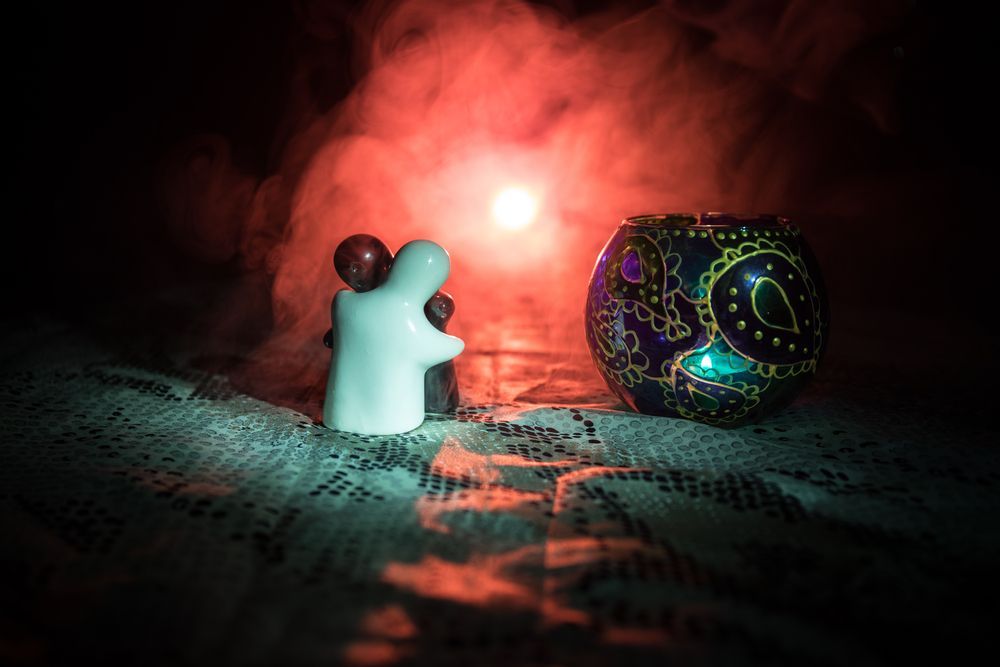 Figura fantasmal que sostiene corazones cerca de un candelabro con un diseño estampado, en un entorno tenue y lleno de humo.