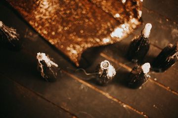 Velas quemadas y una tela de lentejuelas doradas sobre tablones de madera oscura.