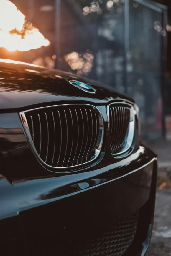 Frontal de coche BMW de color negro con parrilla cromada, iluminado por la luz solar.