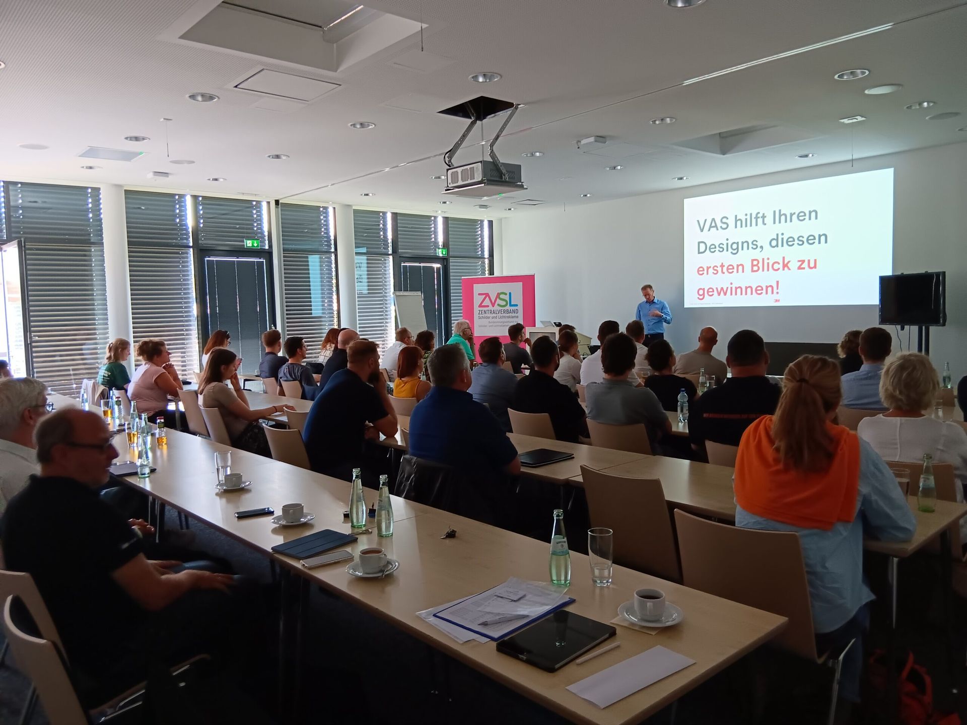 Ein Mann hält vor einer Gruppe von Menschen in einem Konferenzraum eine Präsentation.