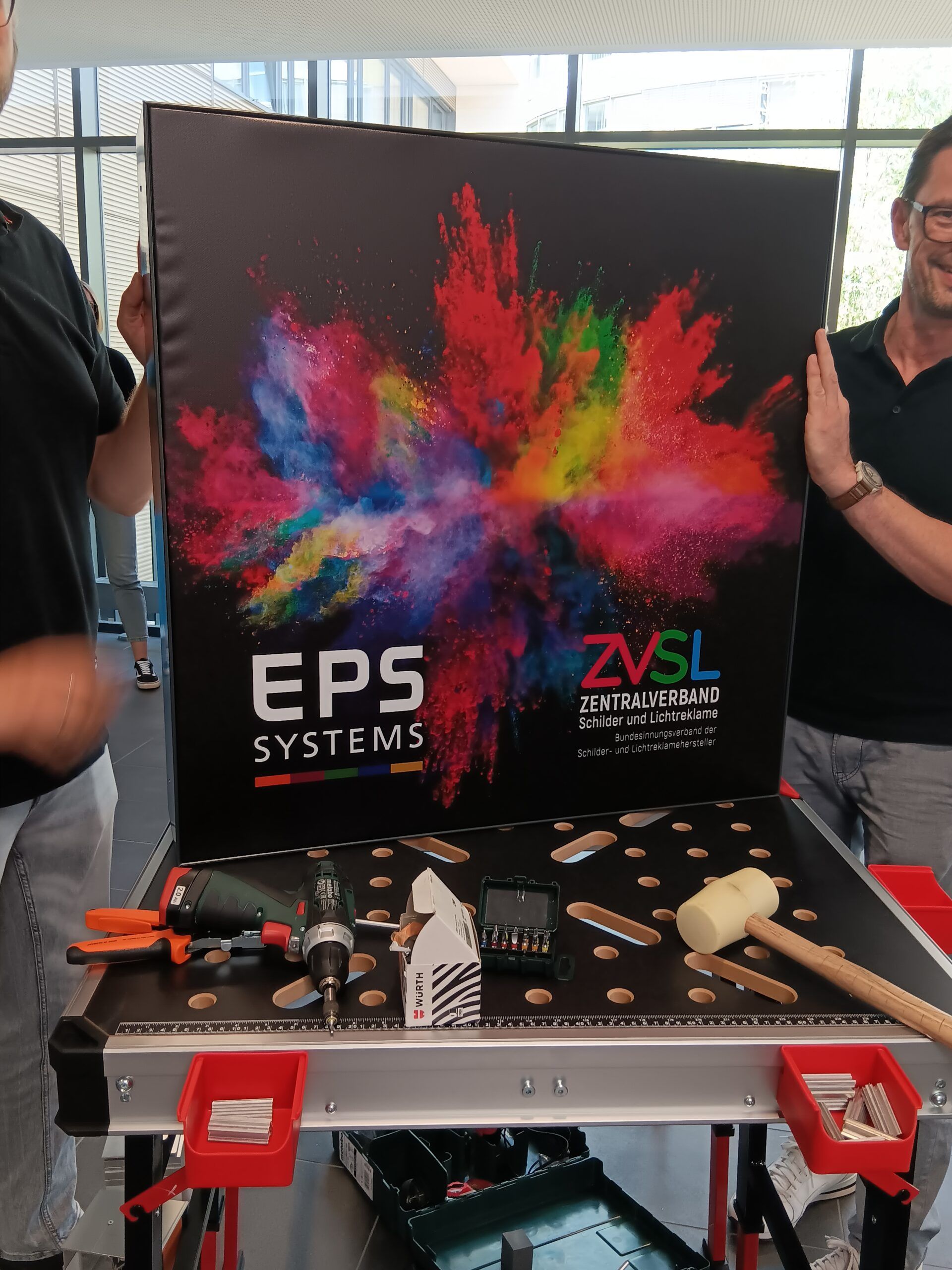 Zwei Männer stehen neben einem Tisch mit einem Schild mit der Aufschrift „EPS Systems“.
