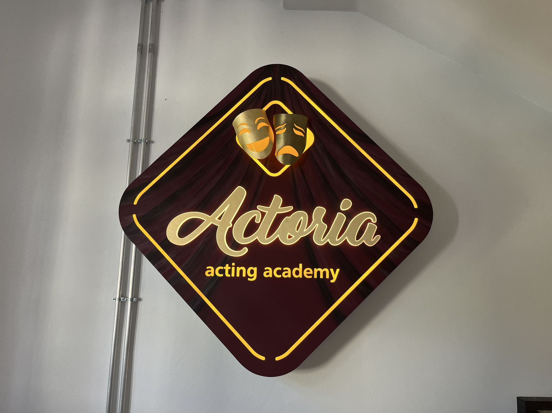 Schild der Adoria Acting Academy an einer Wand, dunkelrot mit goldener Schrift und Theatermasken