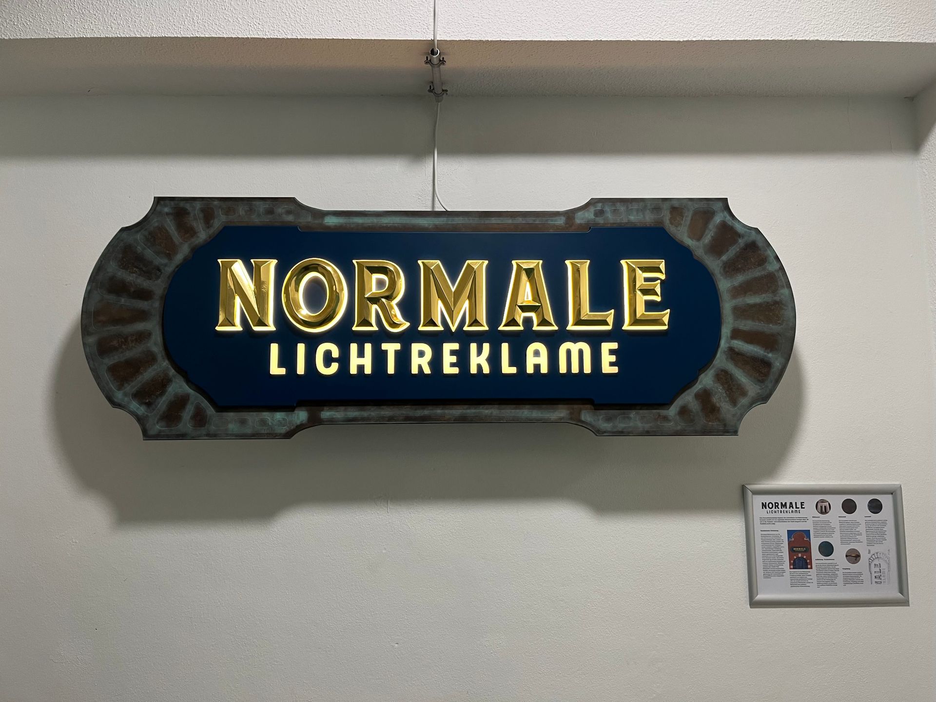 Normale Lichtrikane-Schild an einer Wand mit goldener Schrift auf blauem Hintergrund