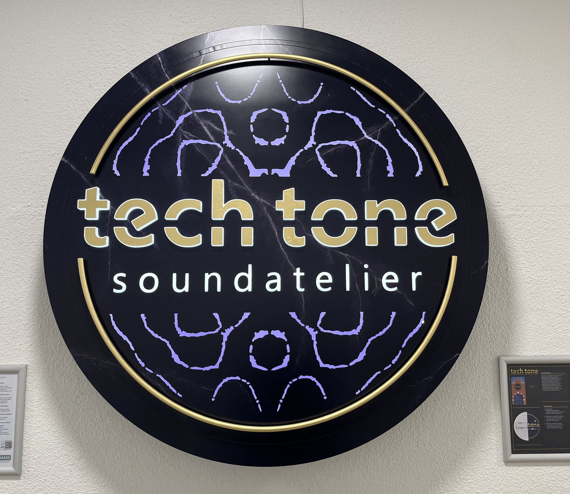 Rundes schwarzes Neonschild mit der Aufschrift „tech tone soundatelier“ in Gelb und Lila.