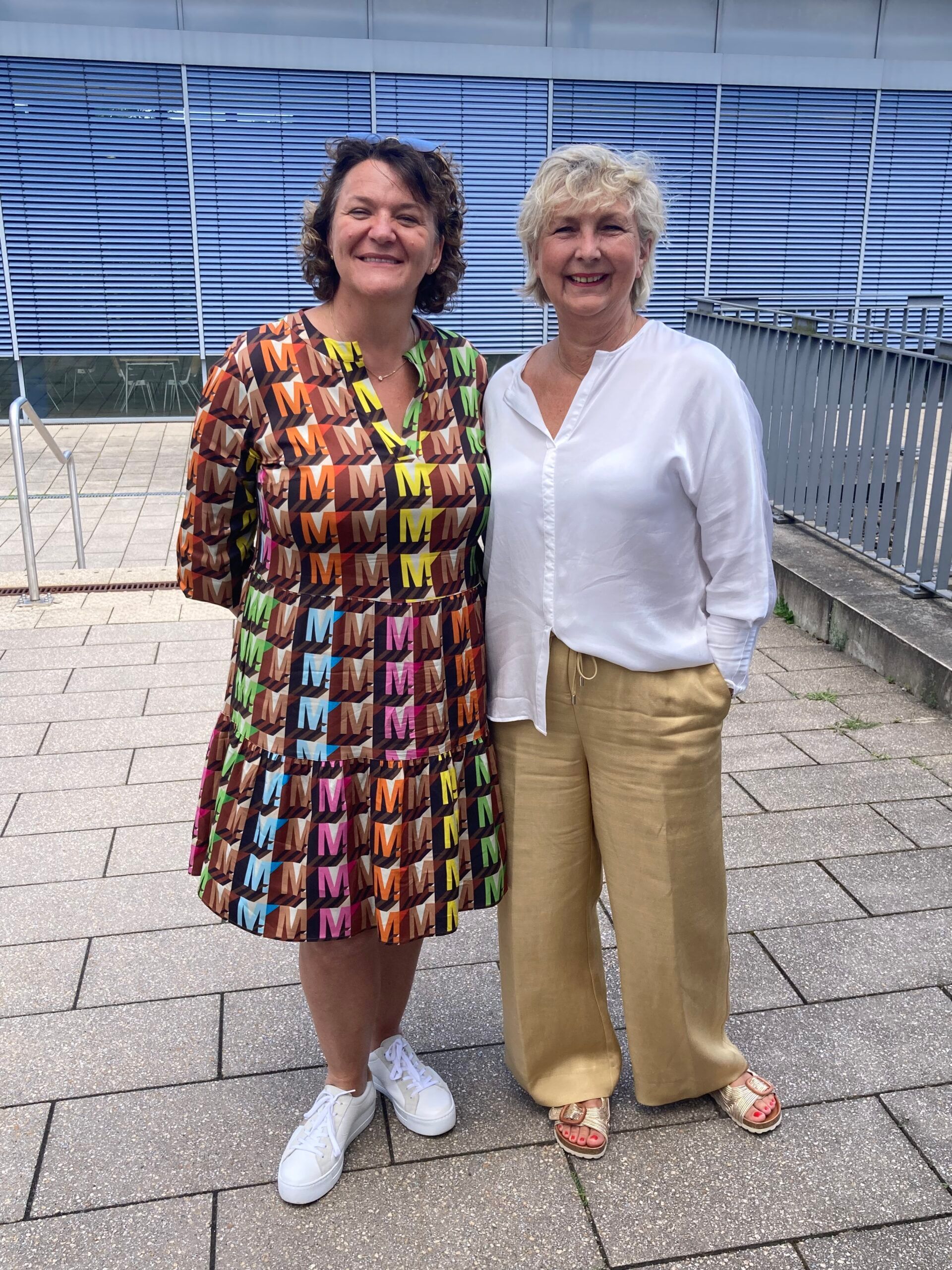 Zwei Frauen stehen nebeneinander auf einem Bürgersteig.