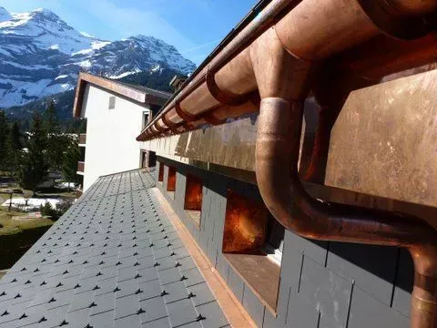 Une gouttière en cuivre sur le côté d'un bâtiment avec des montagnes en arrière-plan