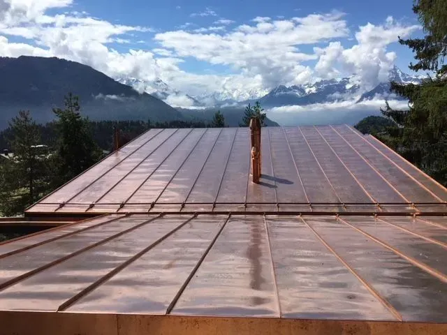 Un toit en cuivre avec une cheminée au-dessus et des montagnes en arrière-plan.