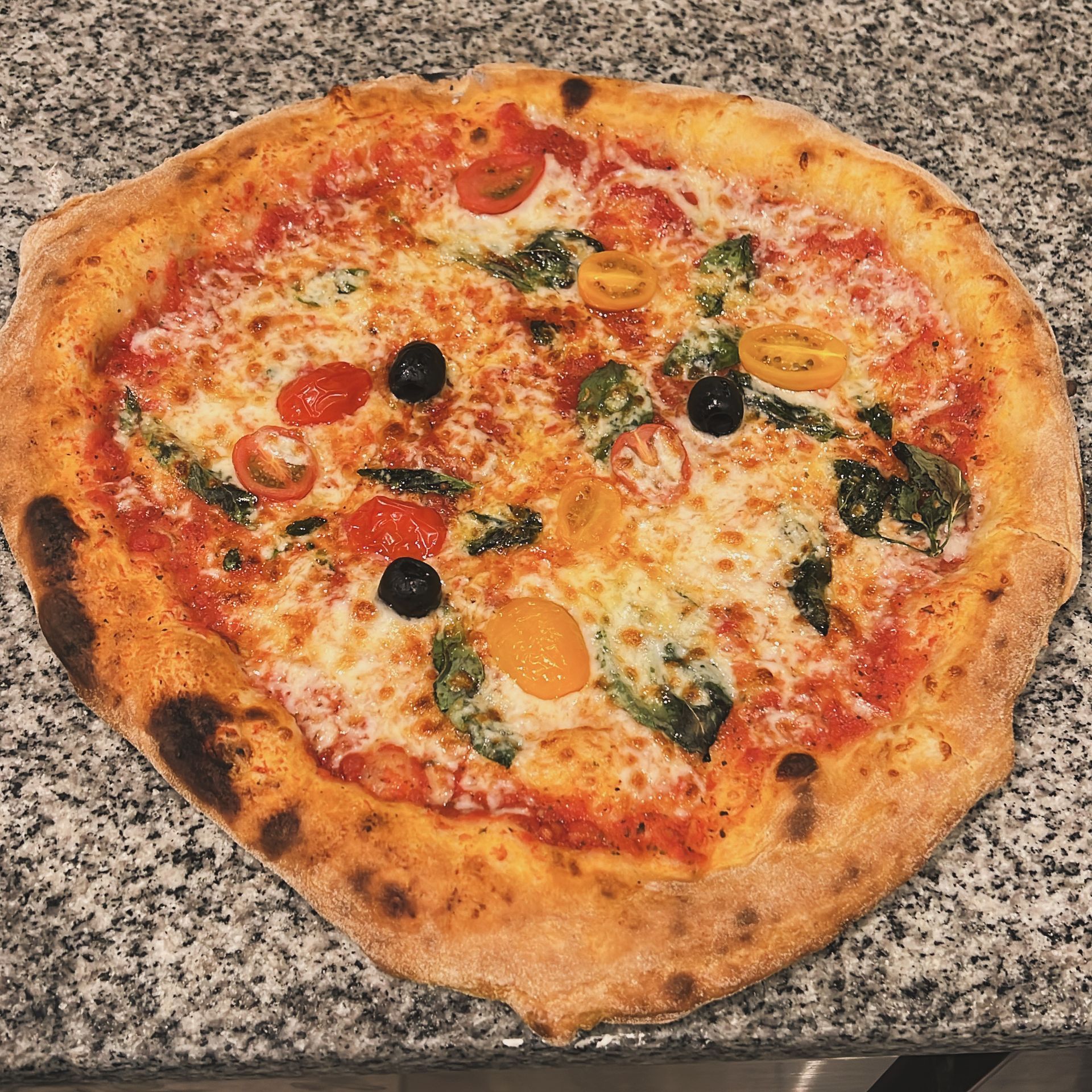 Pizza entière avec sauce tomate, fromage, olives et herbes sur un comptoir.